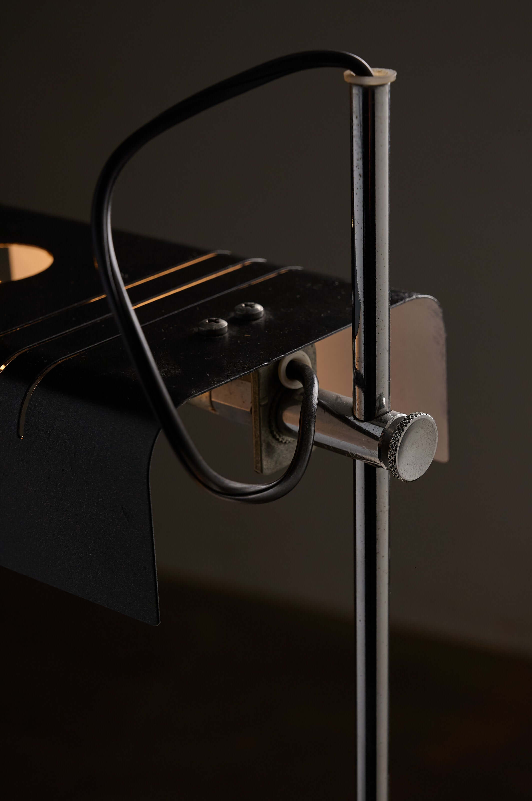 Close-up of the mechanism of an adjustable chrome desk lamp with black metal shade and tubular chrome stem.