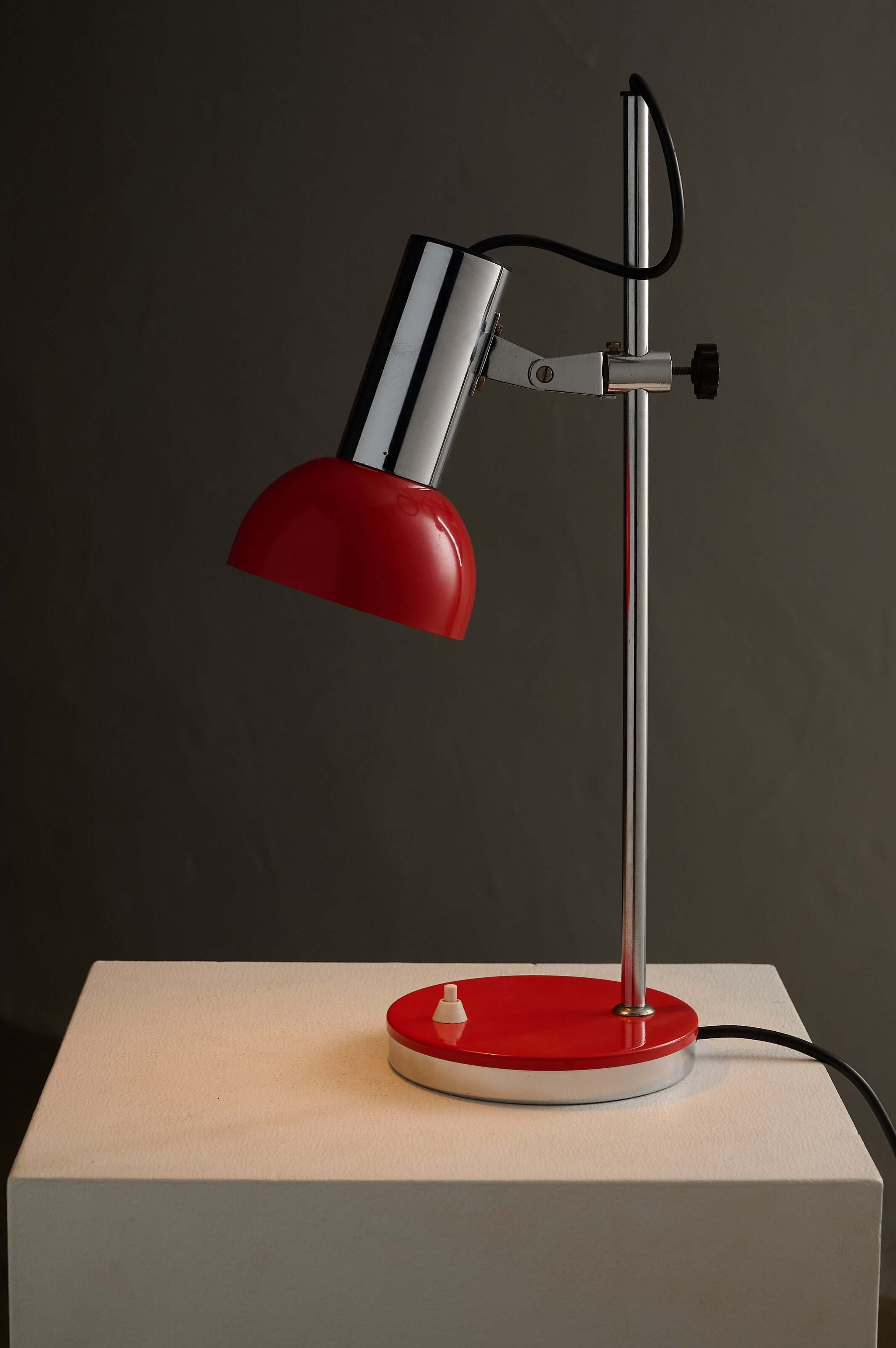 Adjustable Chrome and Red Space Age Table Lamp with a chrome rod and red shade on a white base.