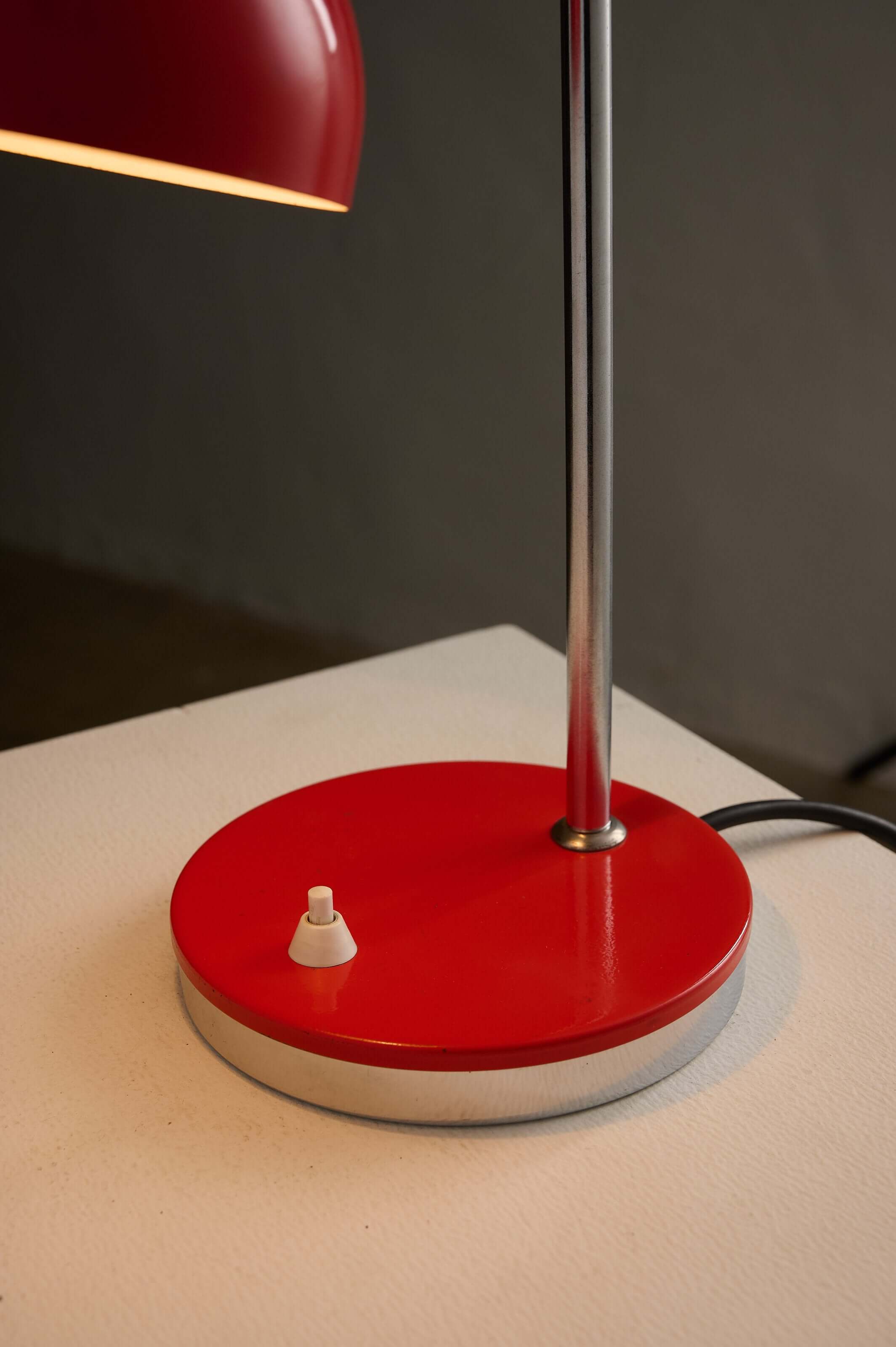 Adjustable chrome red table lamp with a red circular base and simple white switch.