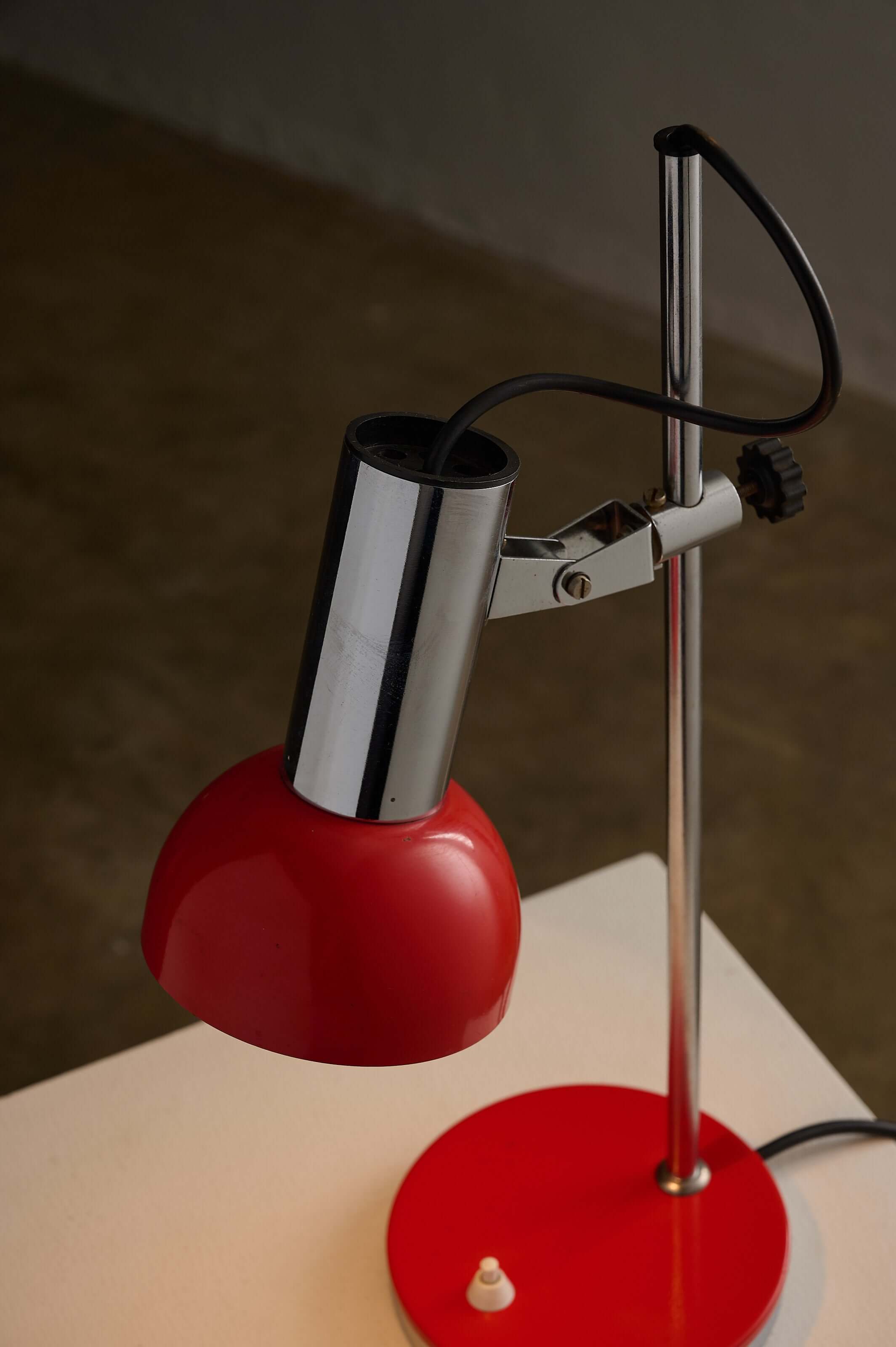Adjustable chrome red table lamp with a red hemispherical shade and chrome housing, perfect for stylish illumination.