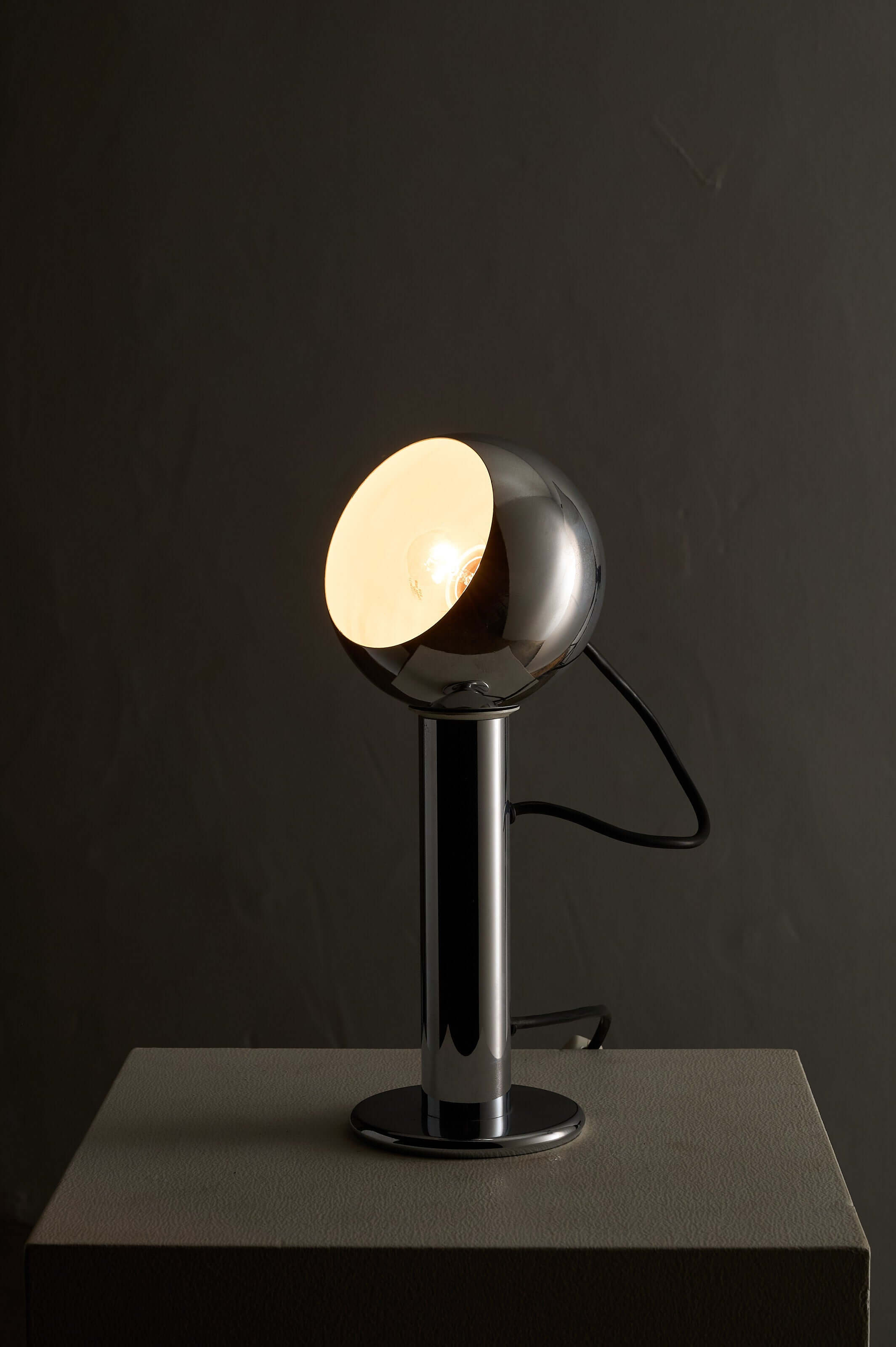 Adjustable chrome table lamp featuring a spherical shade on a cylindrical base, designed for versatile lighting.