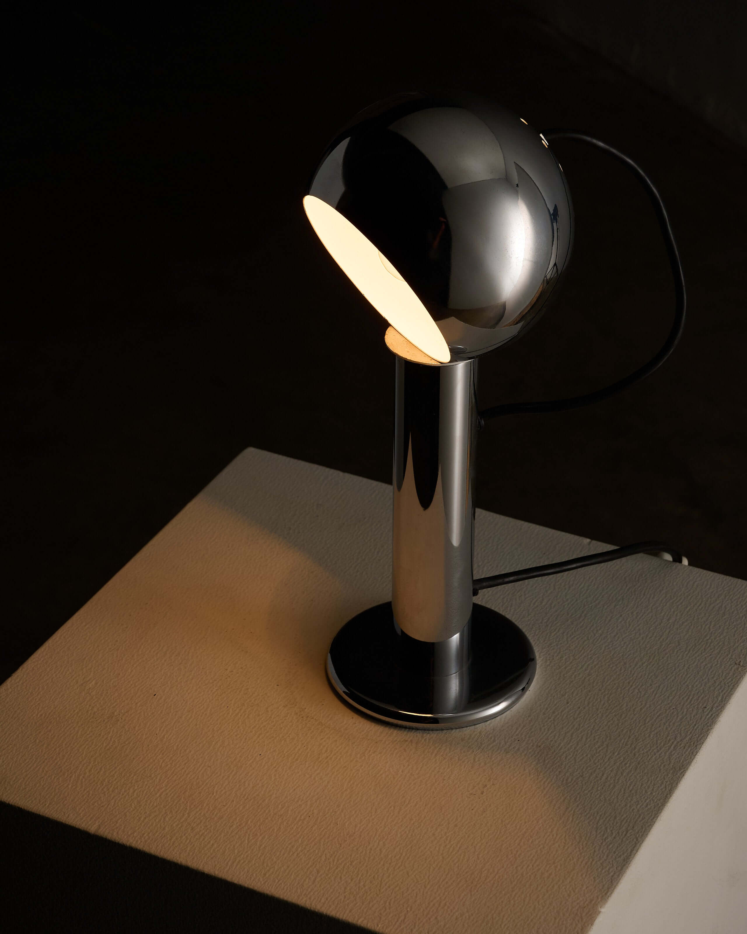 Adjustable chrome table lamp with a spherical shade and cylindrical base, providing versatile lighting options.