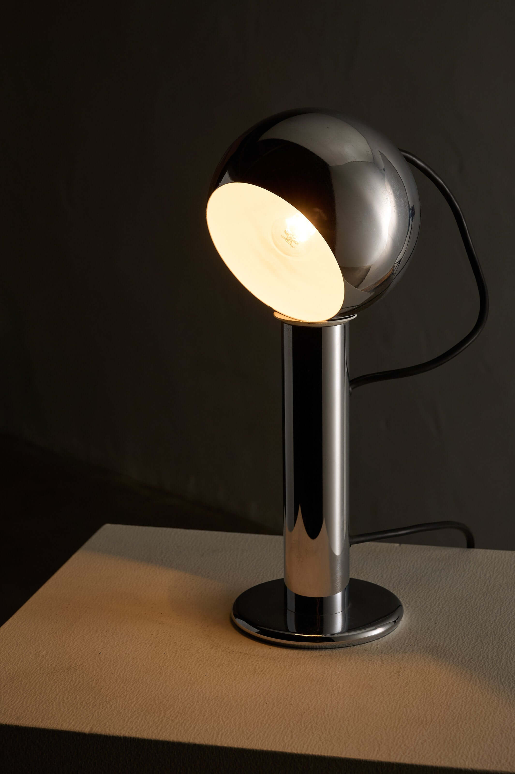 Adjustable chrome table lamp featuring a spherical shade and cylindrical base with a reflective finish.