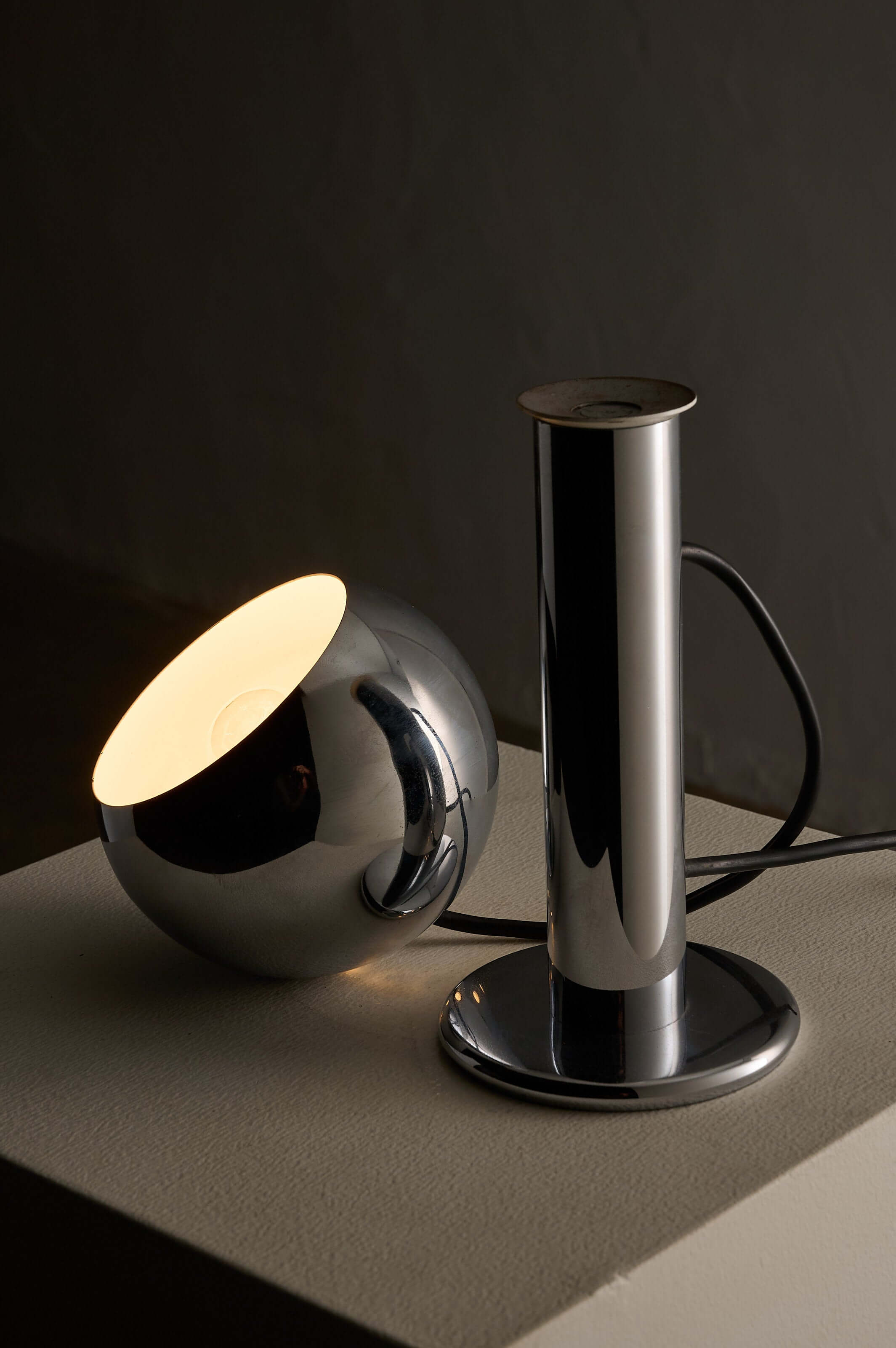 Adjustable chrome table lamp with spherical shade and cylindrical column design.
