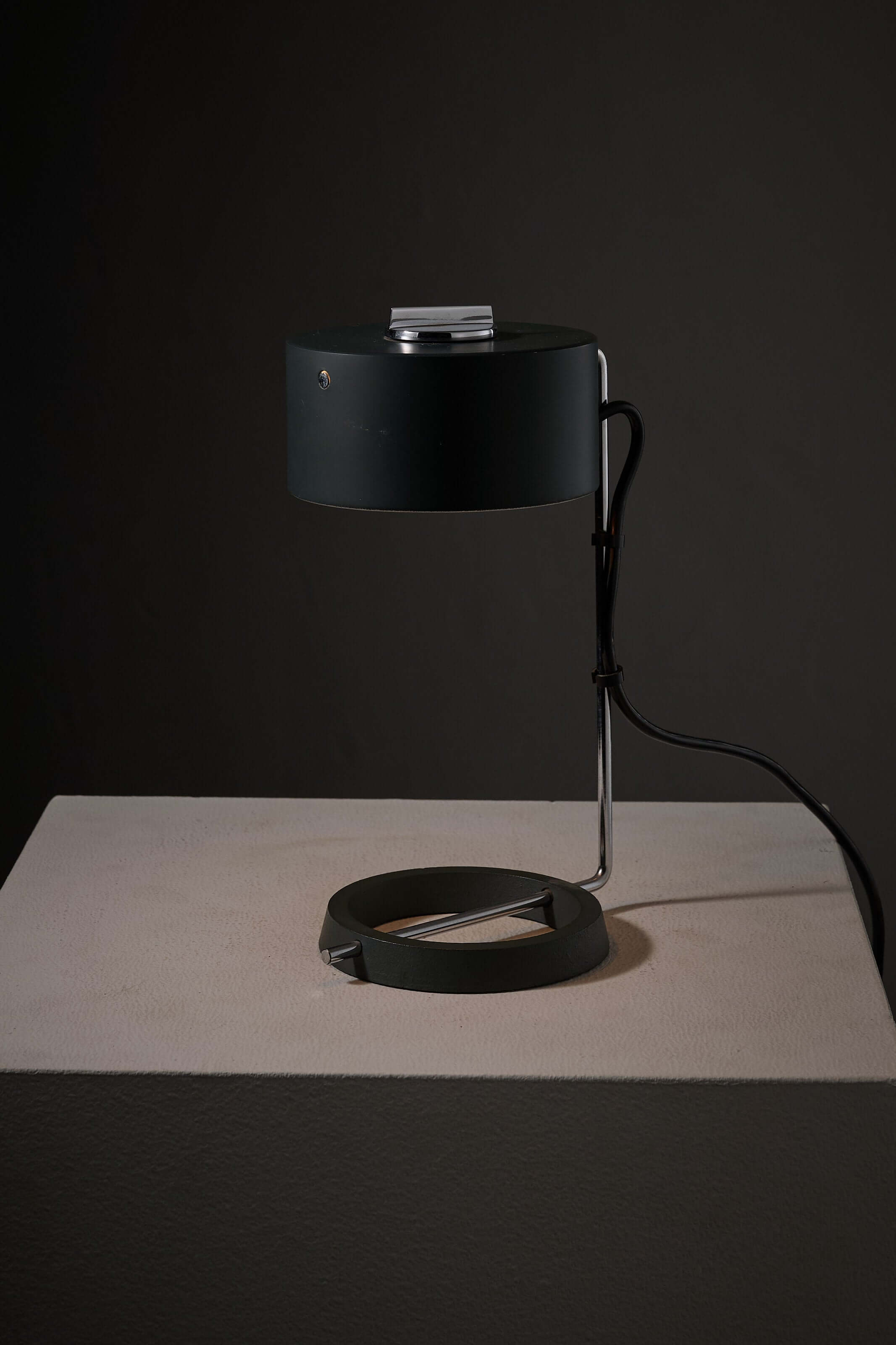 Adjustable minimalist desk lamp with an anthracite base and chrome stem, featuring a round shade and dial for light adjustment.