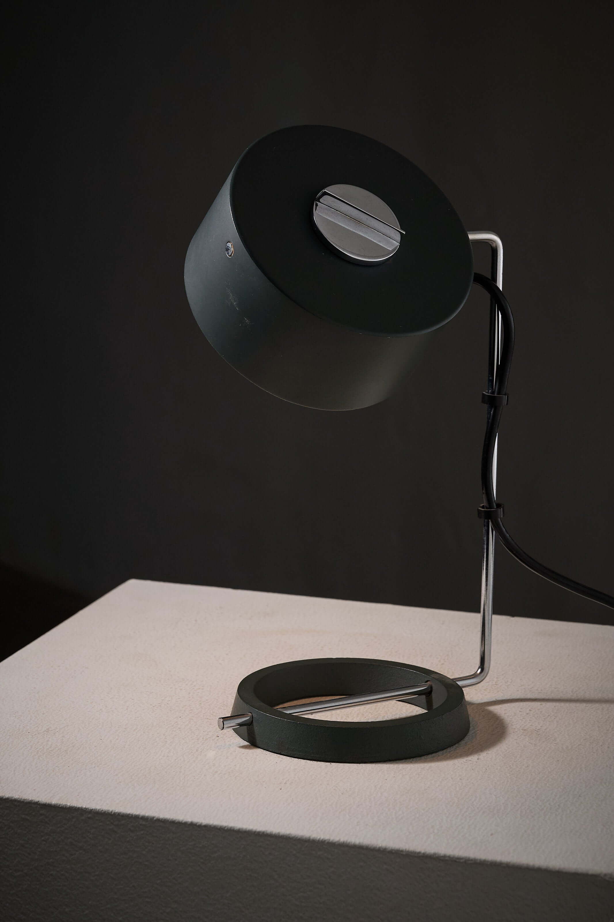 adjustable minimalist desk lamp with anthracite and chrome finish on a white pedestal