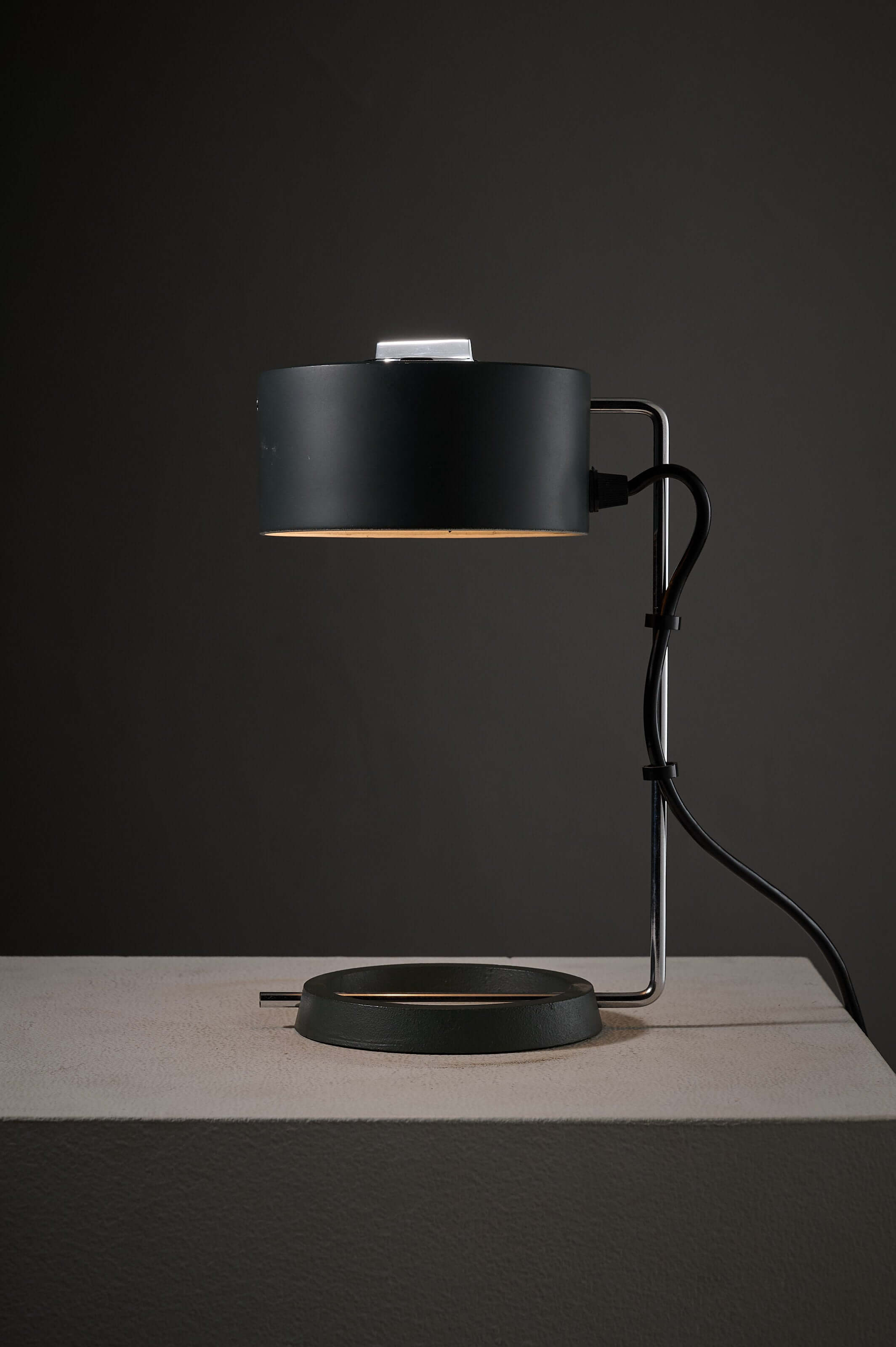 Minimalist anthracite and chrome adjustable desk lamp with ring base on a table.
