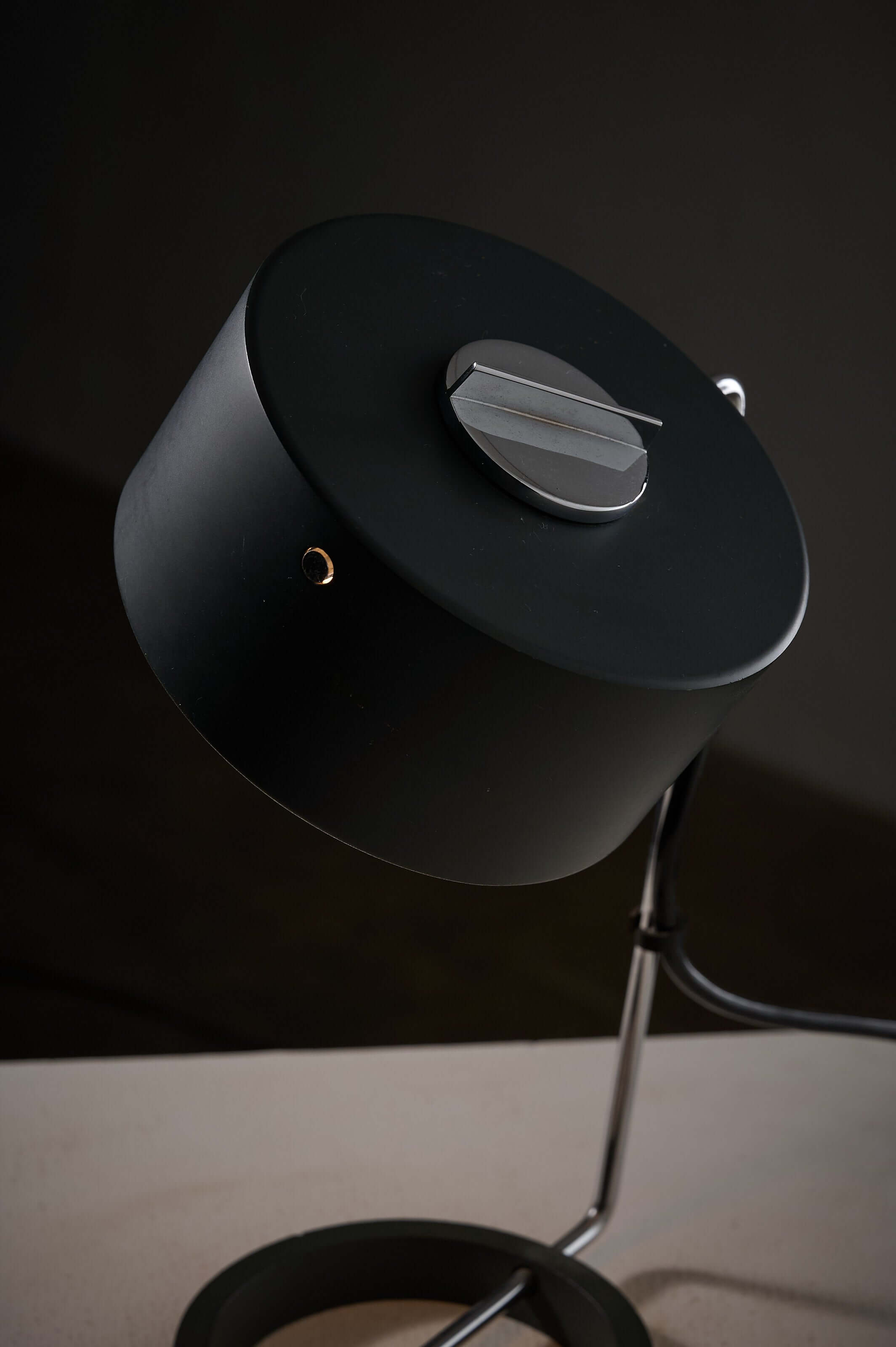 Adjustable minimalist desk lamp with black cylindrical shade and chrome dial, featuring a stable ring base.