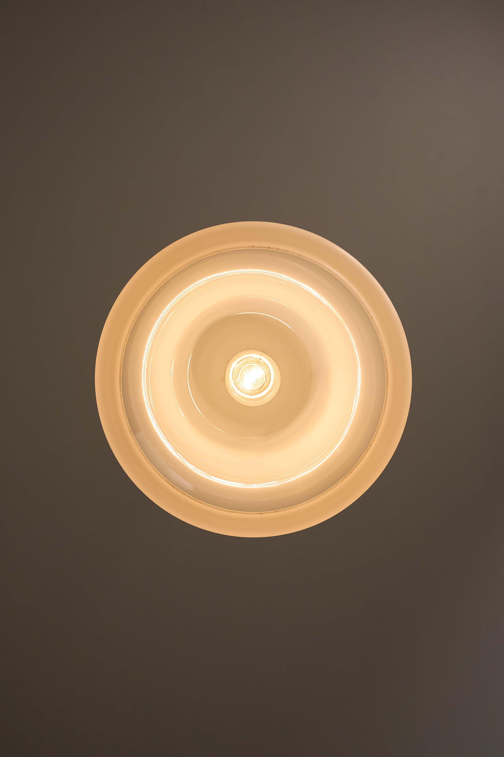 Mid-century opaline glass pendant light with a polished chrome cap, emitting a soft glow from above.