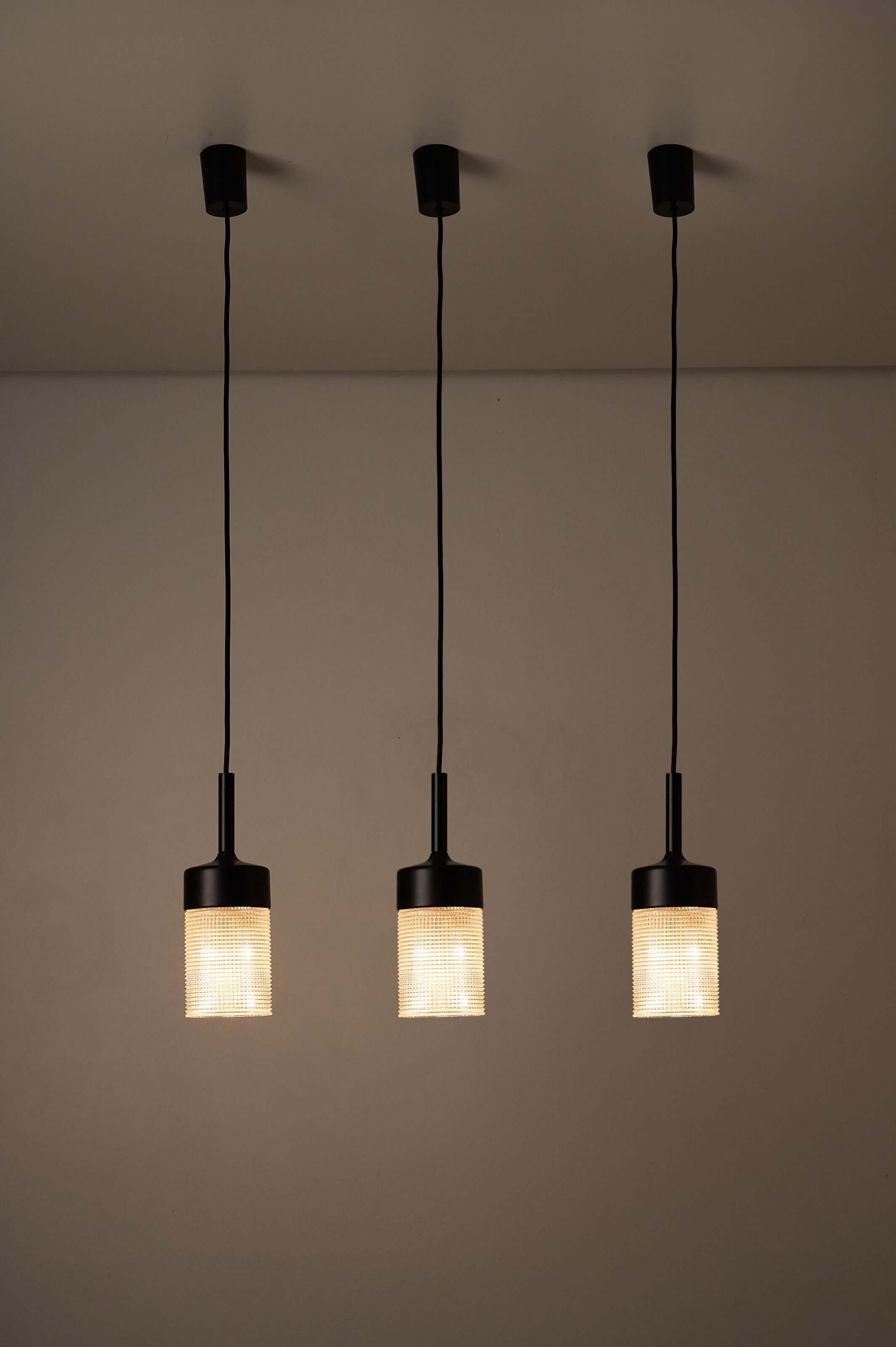 Three pendant lights featuring structured glass pendant light design with matte black metal tops.
