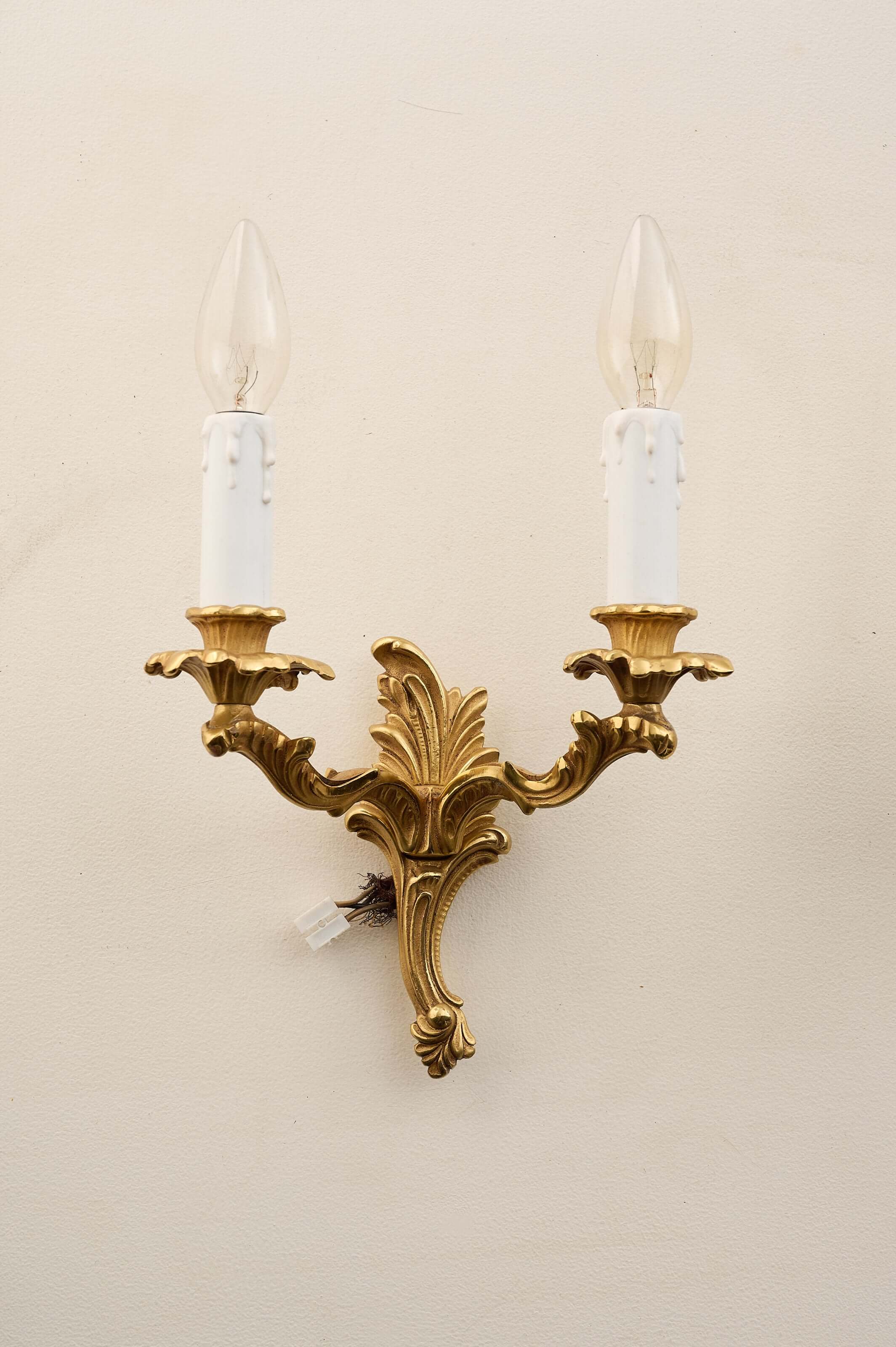 Louis XV style brass wall sconces featuring double arms, floral bobèches, and faux-candle sleeves.
