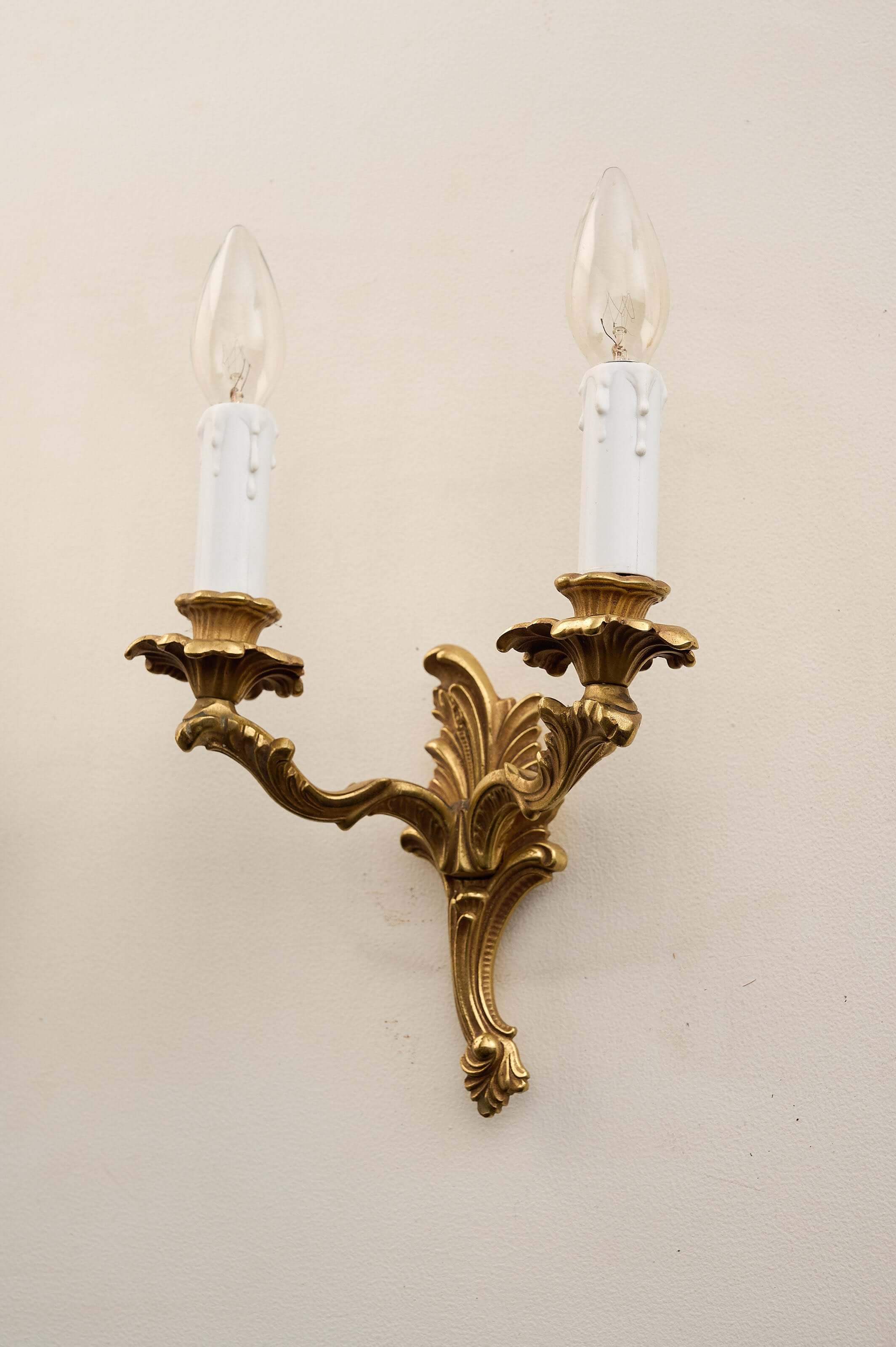 Louis XV style brass wall sconces featuring ornate design and two candle sleeves.
