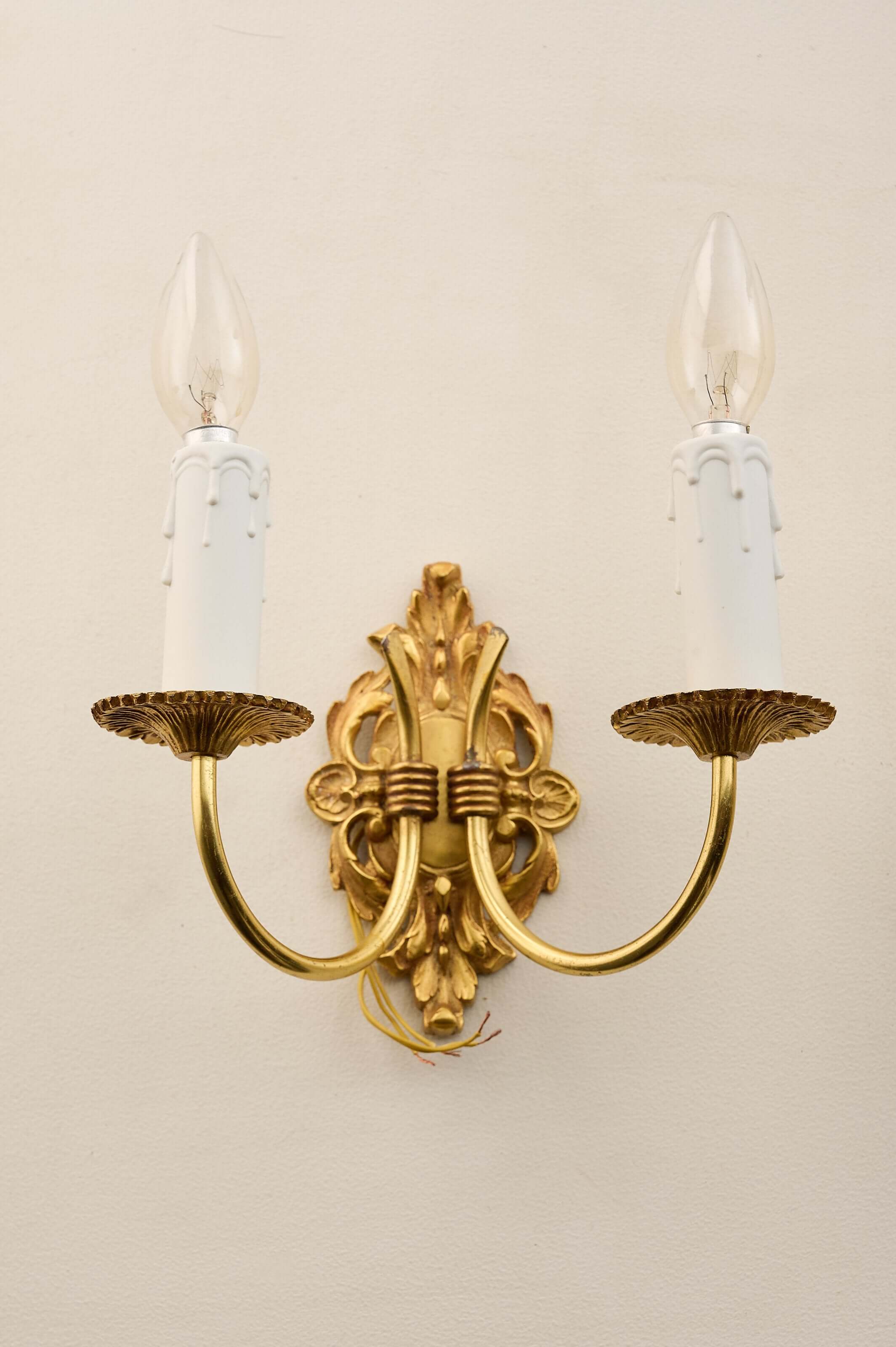 Empire style brass wall sconces featuring a cast brass backplate and two elegantly curved arms with candle-like bulbs.