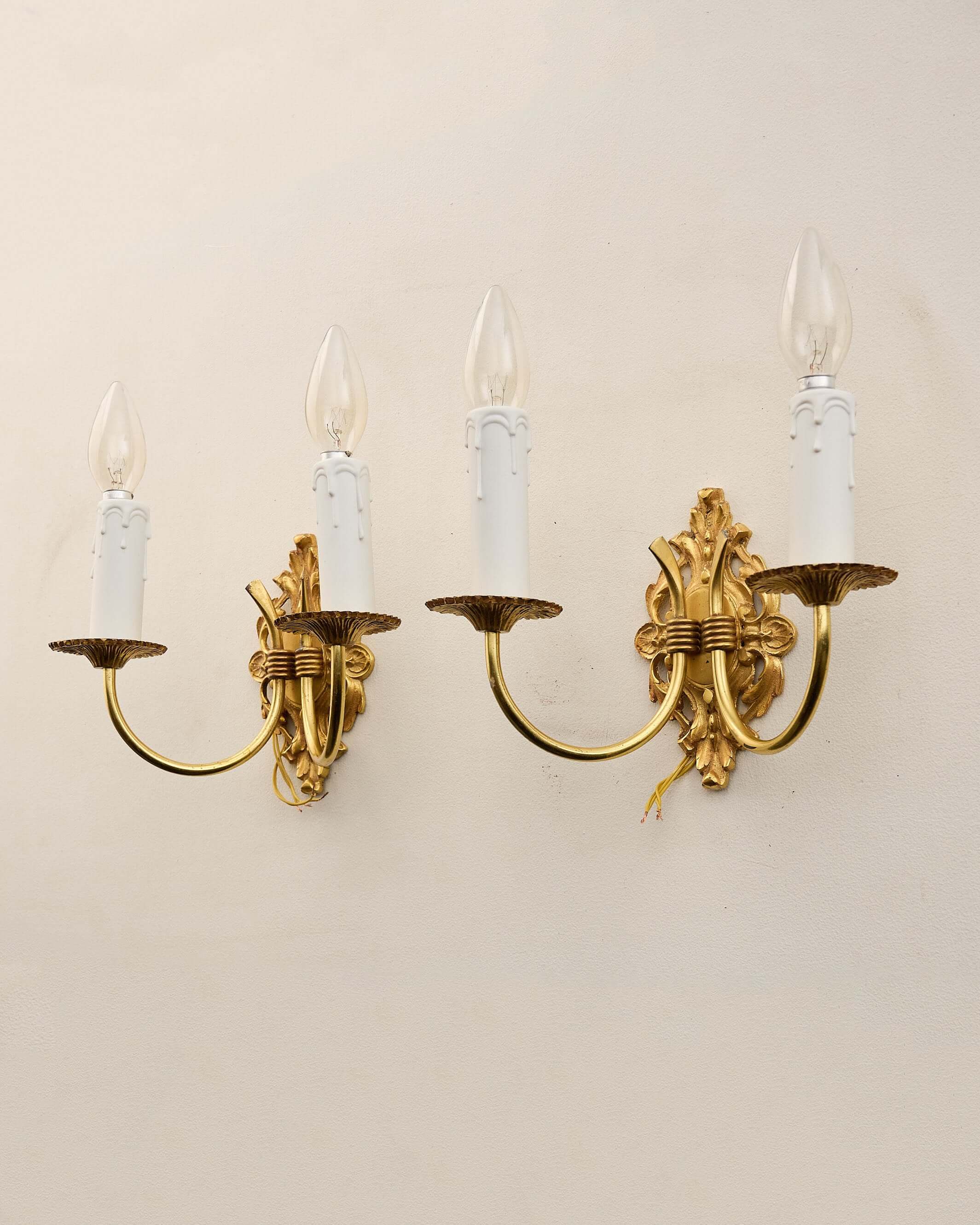 Pair of Empire style brass wall sconces with elaborate backplates and curved arms.