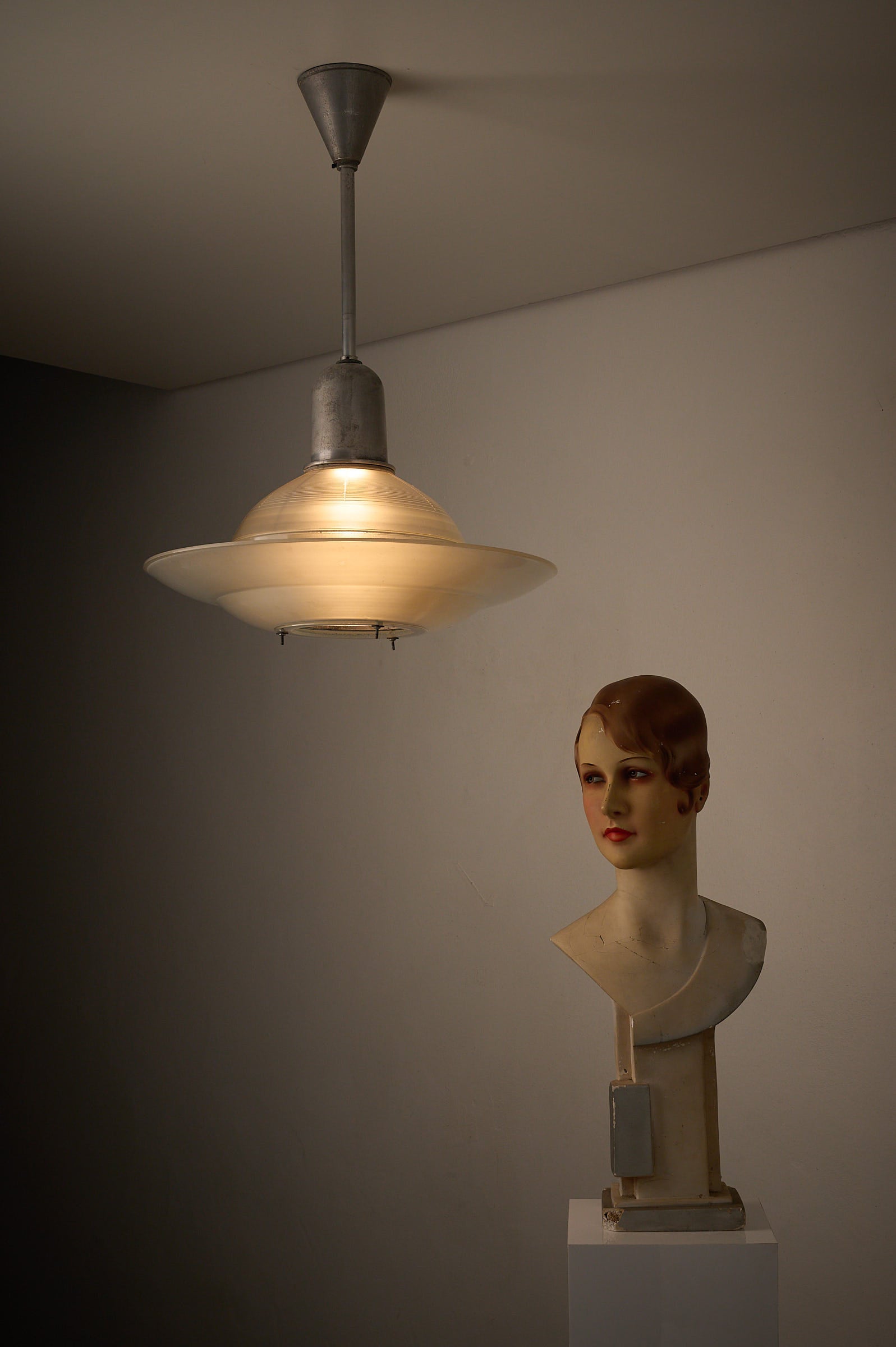 Art Deco Industrial Pendant, 1930s light fixture with frosted glass shade and vintage mannequin head in background.