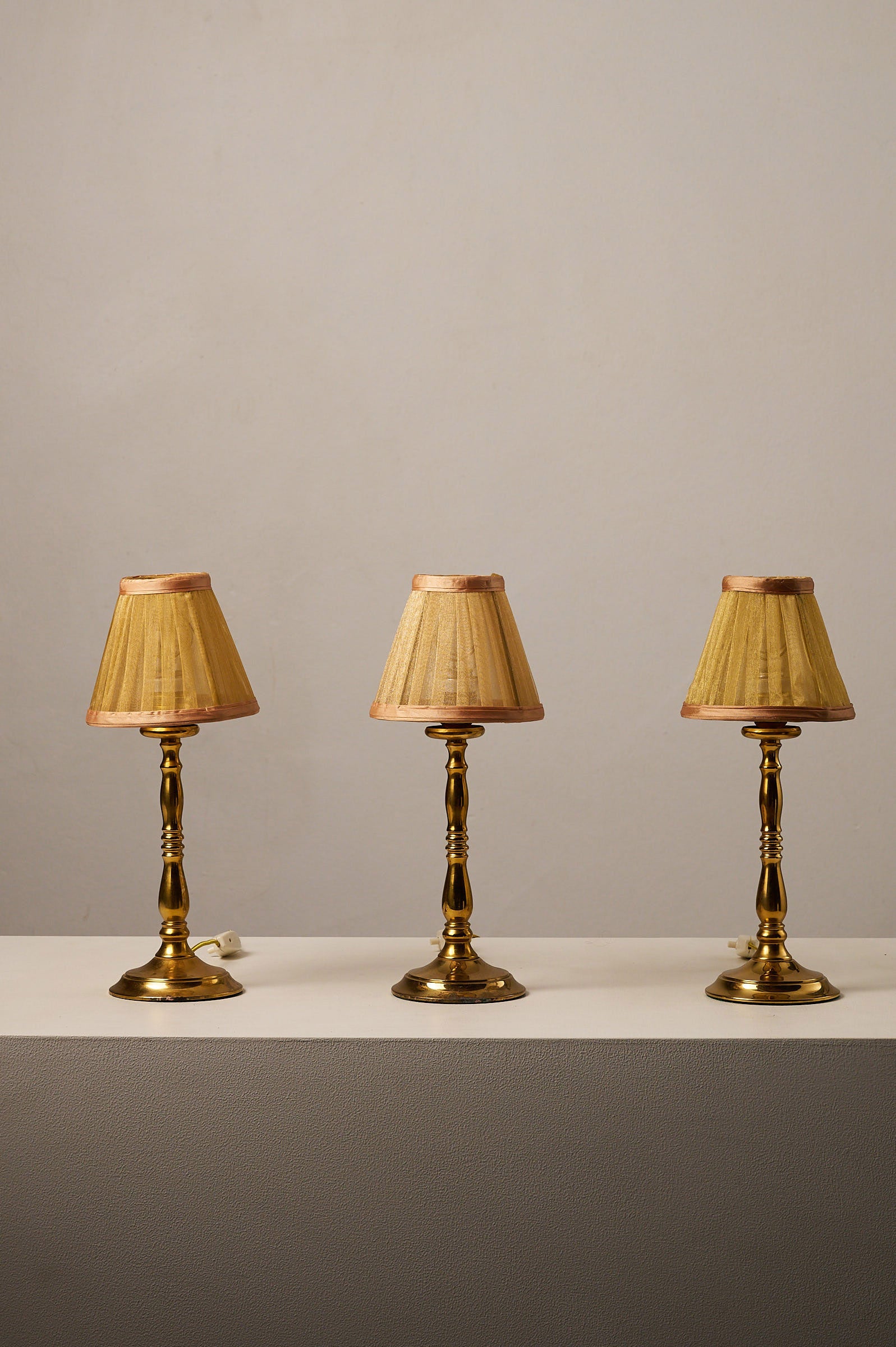Hollywood Regency Brass Table Lamps, Europe, 1970s displayed on a table with pleated shades shining warmly.