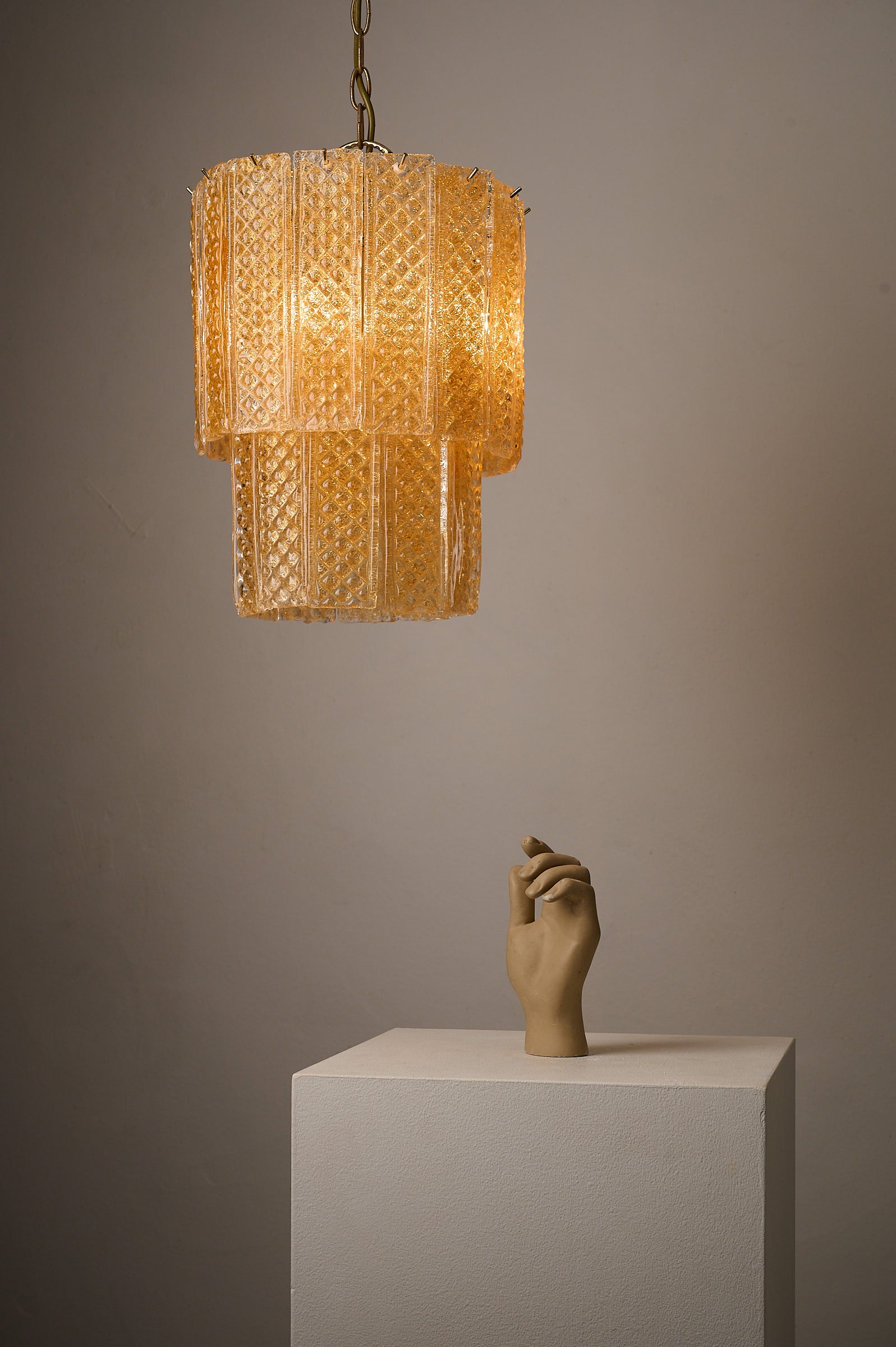Textured Yellow Glass Panel Chandelier, Europe, 1970s hanging above a sculpted hand on a pedestal.