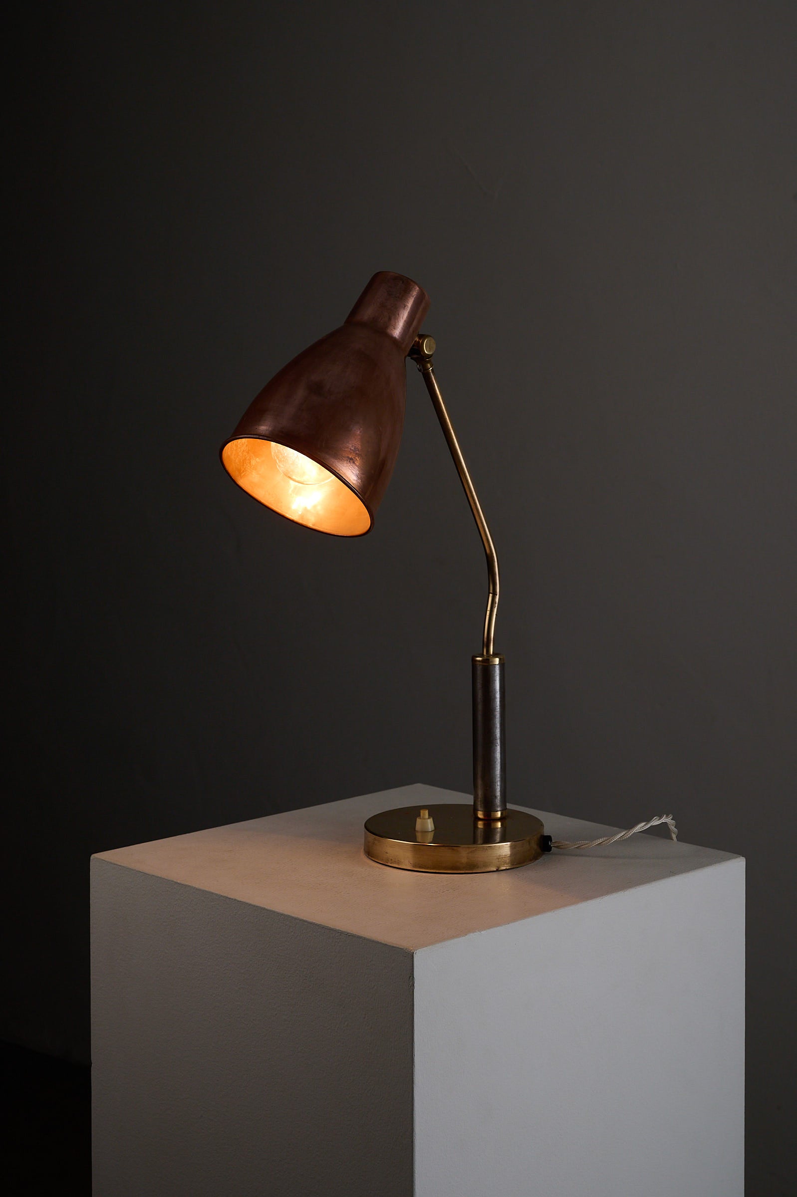 Mid-Century Modern Copper & Brass Desk Lamp, Europe, 1950s on a pedestal with warm light illuminating its design.