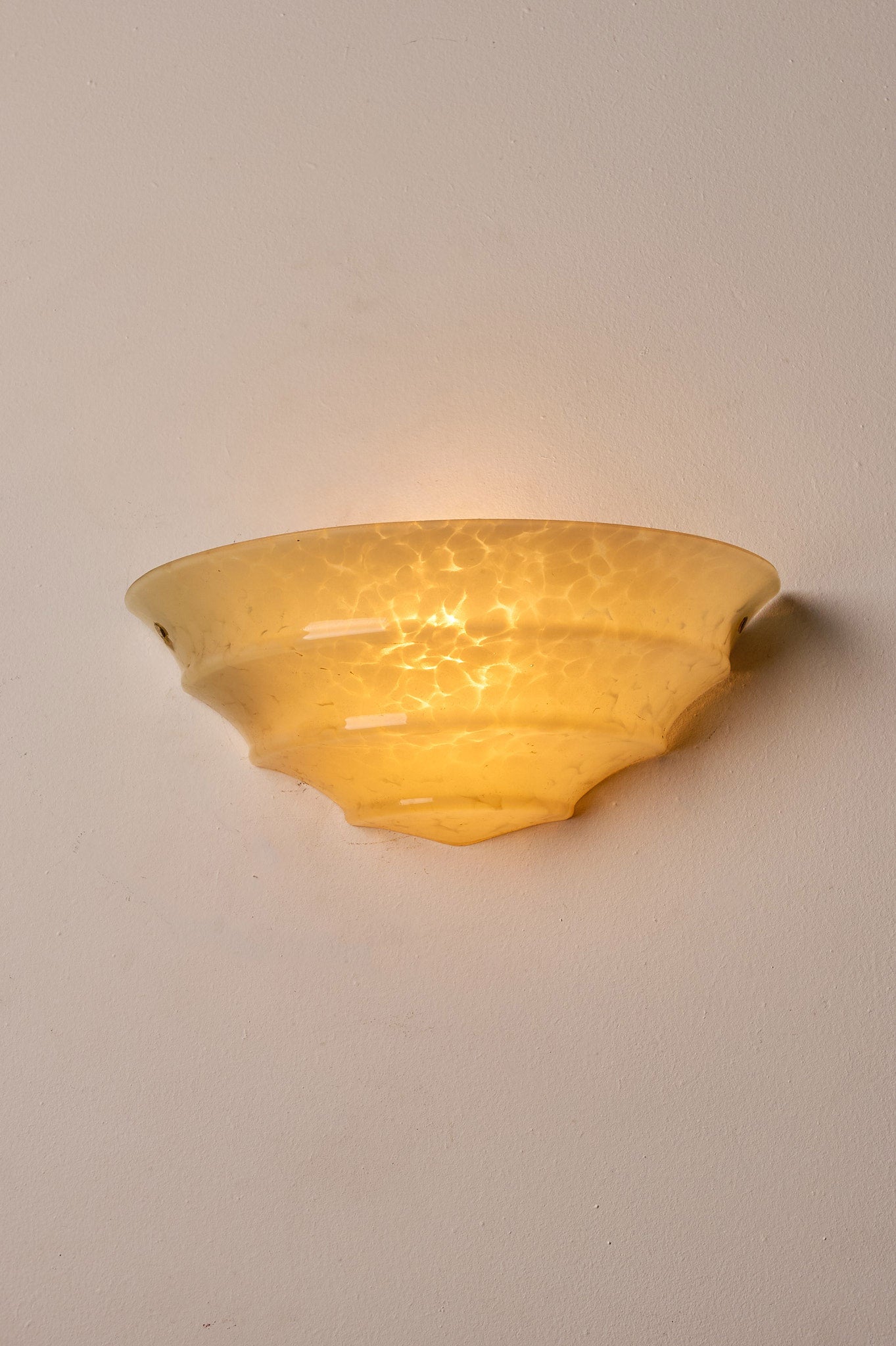 1970s Mid-Century Yellow Marbled Glass Shell Wall Sconce illuminating a wall with soft yellow light.