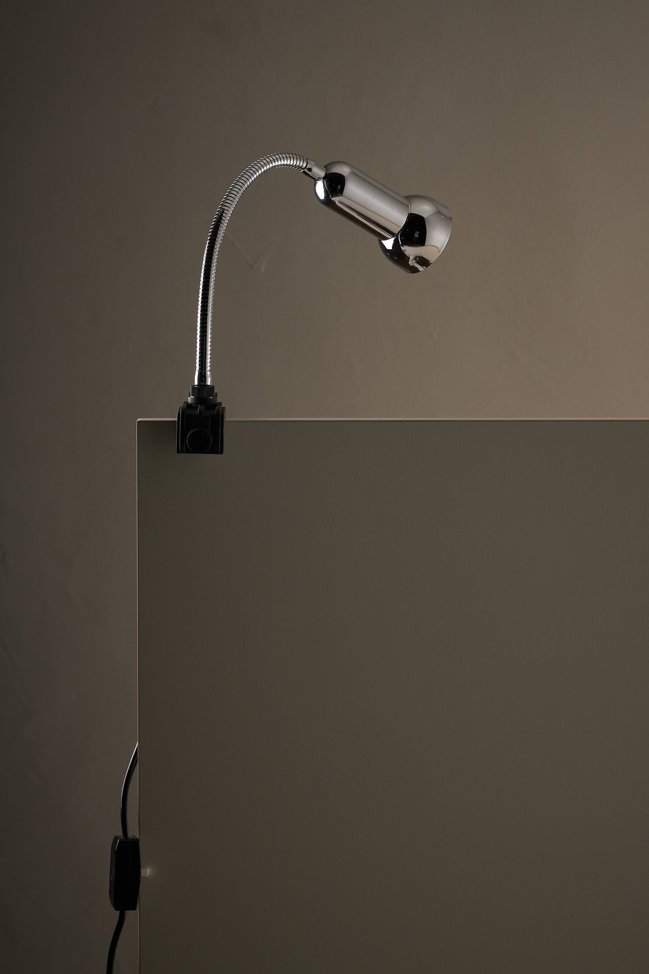 Chrome Clamp Lamp by Cosack mounted on a desk, showcasing its polished chrome and flexible gooseneck design.