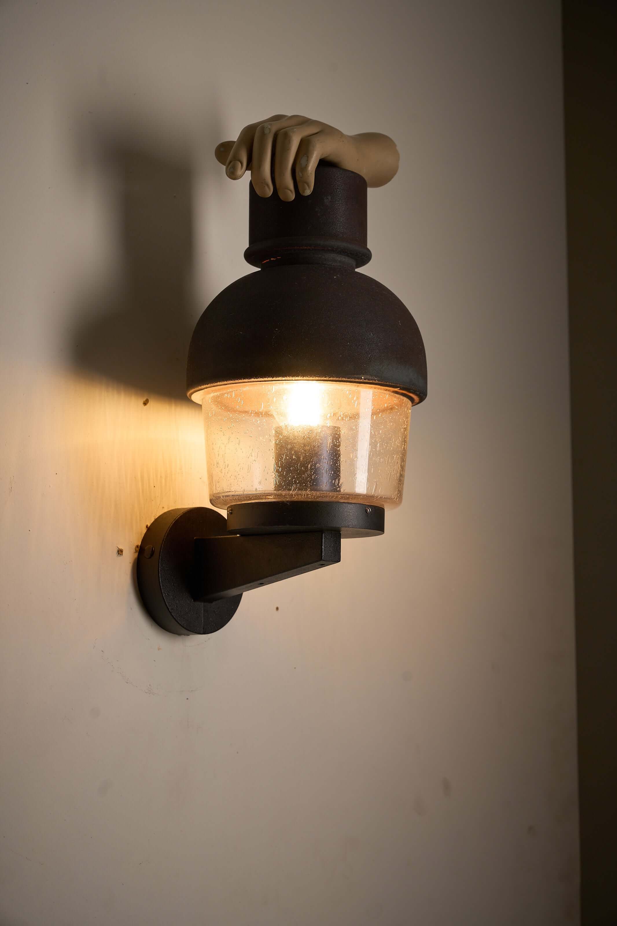 'Boom' Wall Lamp with Fused Copper Alloy on Glass illuminating the wall, featuring a unique hand-shaped design.
