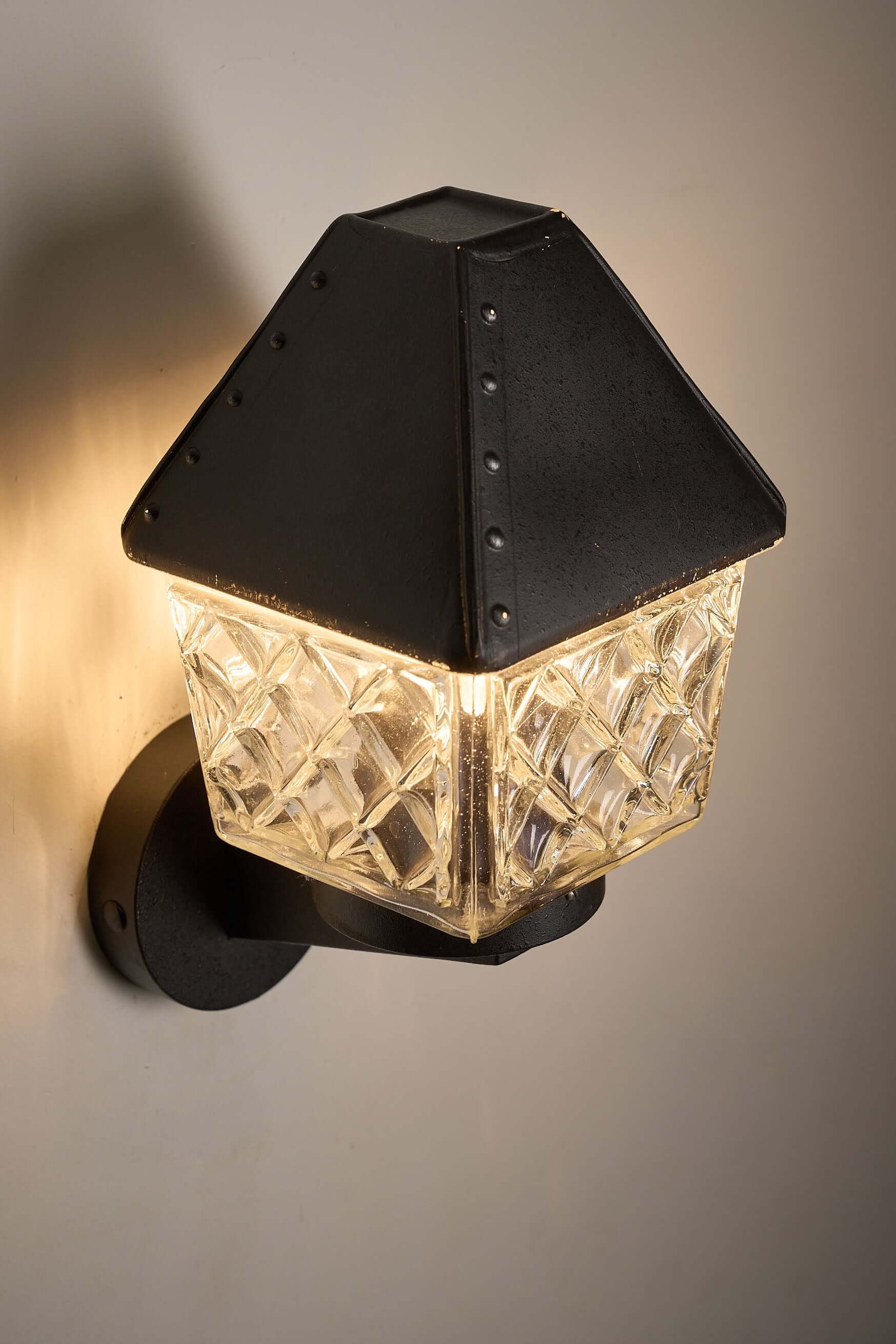 Outdoor Lantern Wall Lamp by Boom Bega illuminating a wall with its geometric glass diffuser and cast aluminium bracket.
