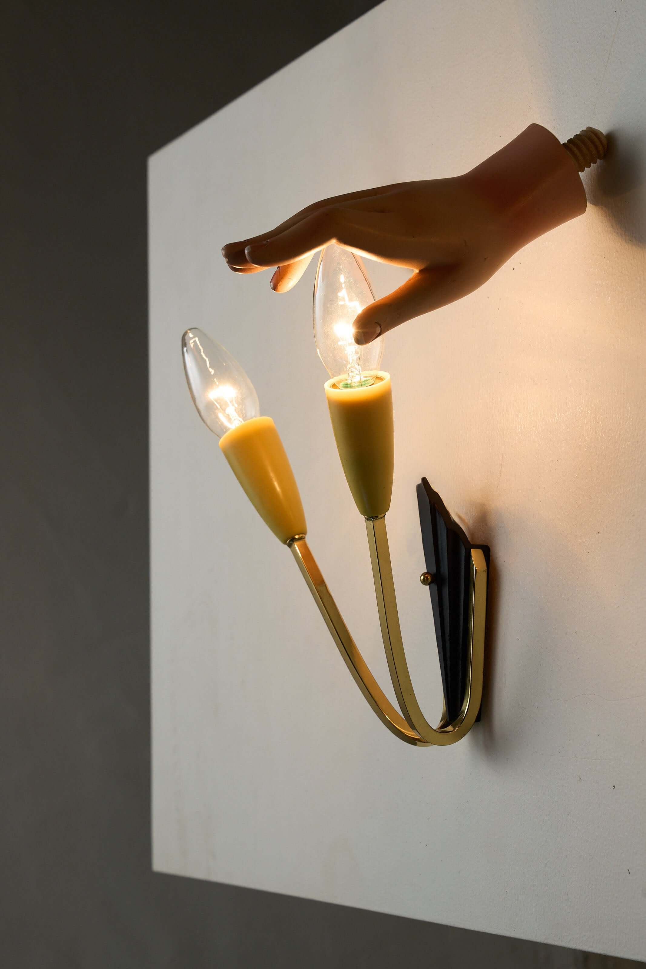 Geometric Brass and Black Wall Lamp, 1950s with a hand holding two cone-shaped light sockets.
