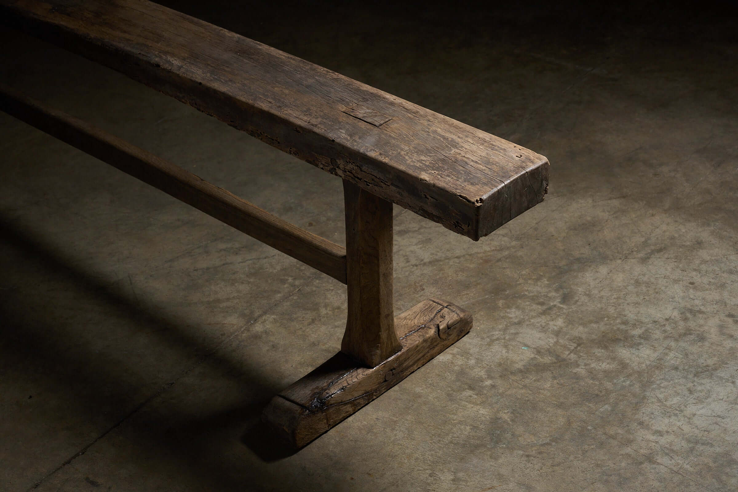 Spanish Trestle Bench in Solid Wood showcasing thick, rustic planks and sturdy T-shaped legs with a weathered patina.