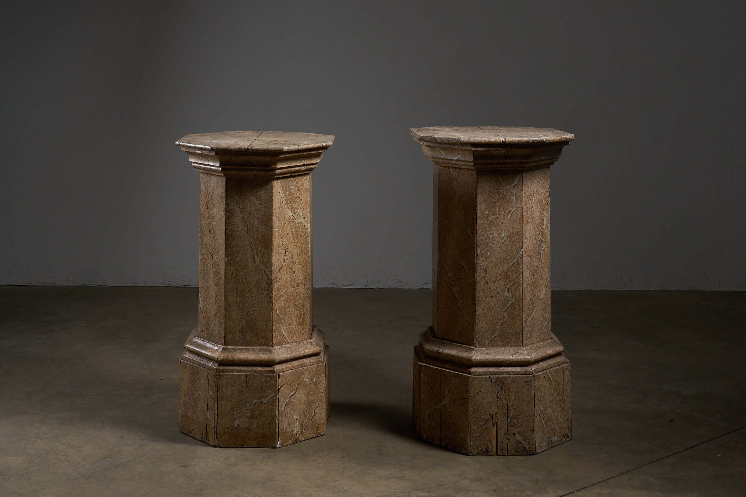 Pair of Antique Faux Marble Octagonal Pedestals in a dimly lit setting, showcasing their unique design and hand-painted finish.