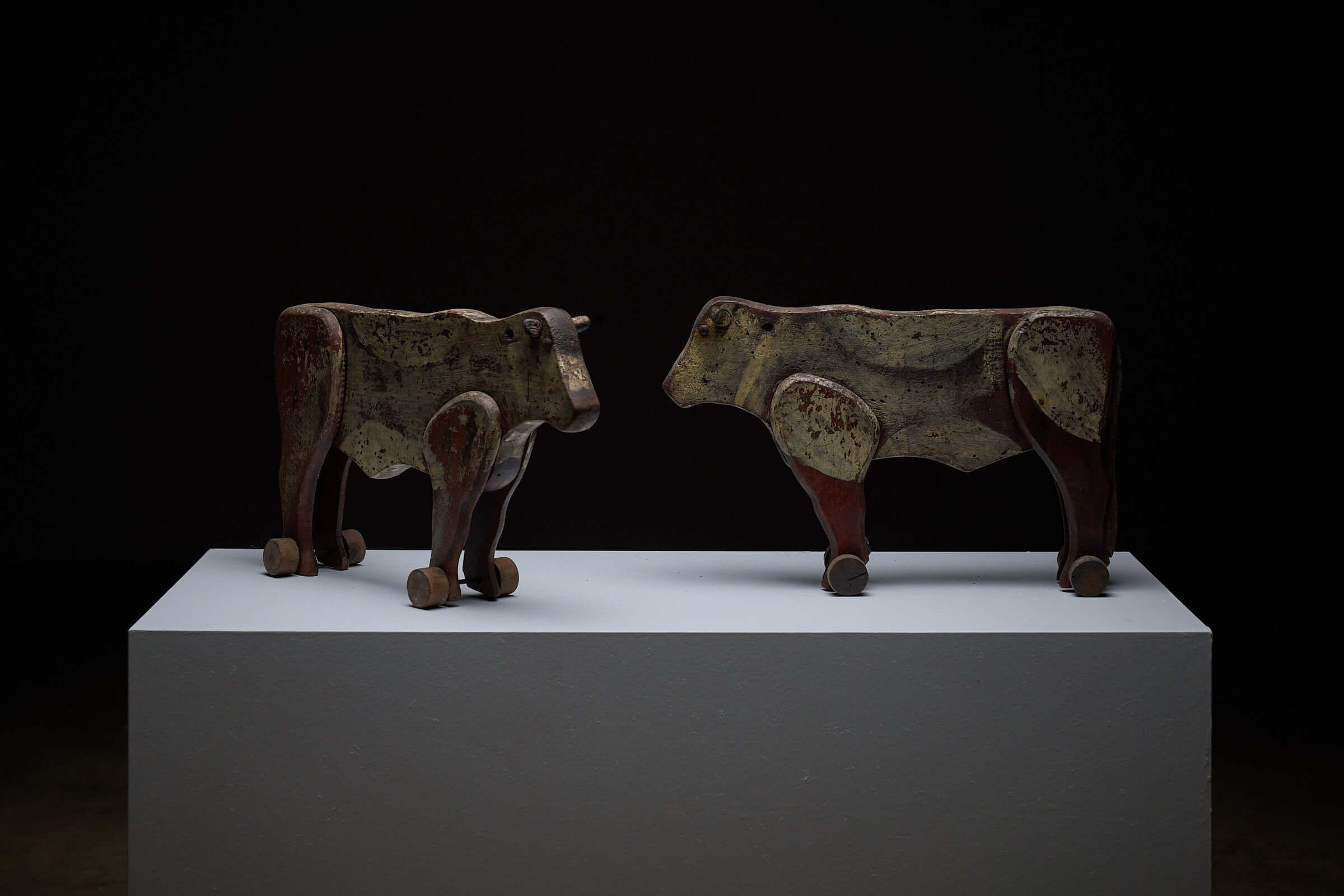Pair of Antique Articulated Wooden Cow Pull Toys displayed on a pedestal, showcasing their distressed antique condition.