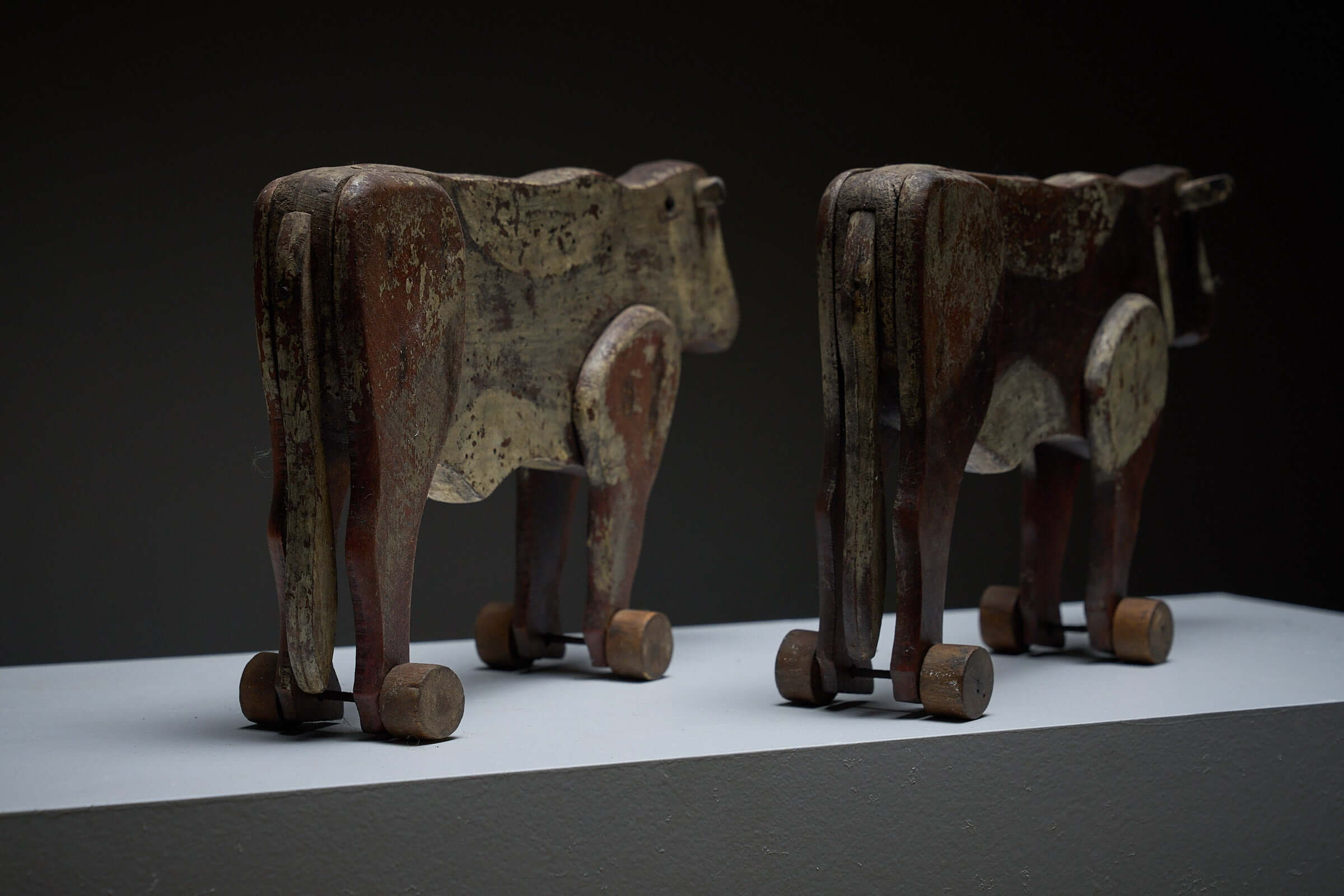 Pair of Antique Articulated Wooden Cow Pull Toys displayed on a pedestal, showcasing vintage folk art craftsmanship.