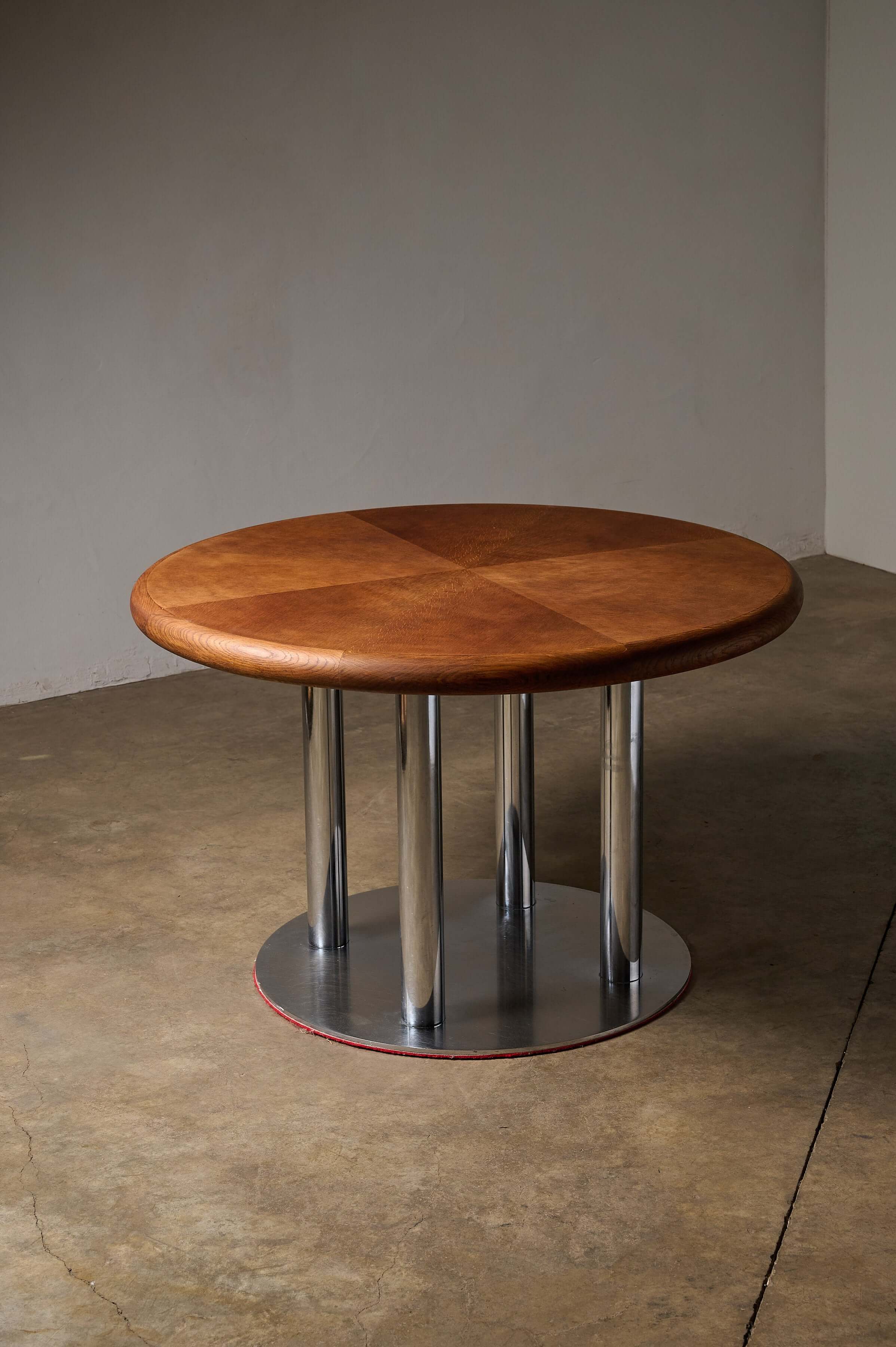 Round 1970s Dining Table with Chrome Pillar Base on a concrete floor, showcasing a wooden top and chrome pillars.