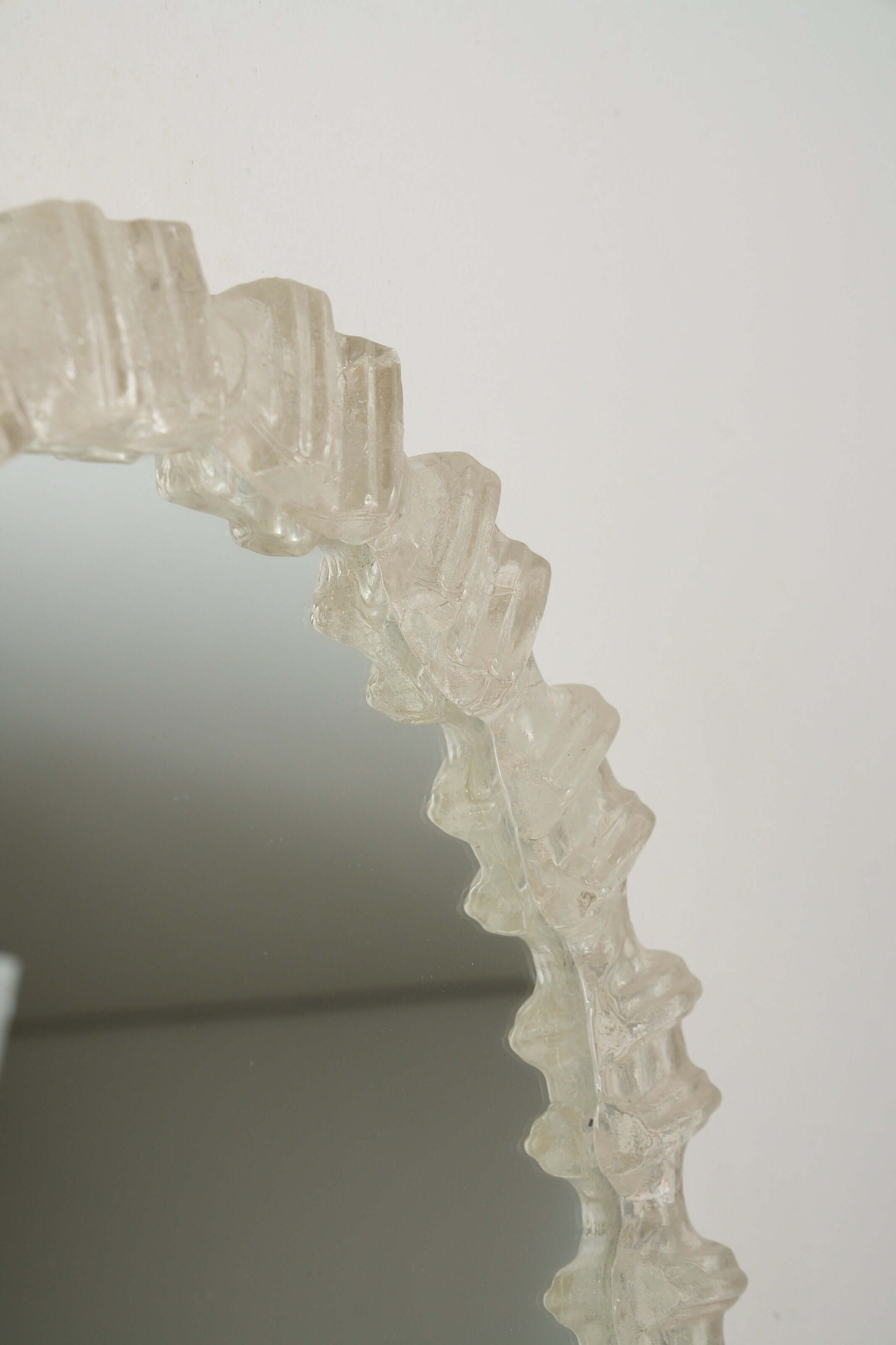 Textured frame detail of an Oval Cast Plexiglass Mirror reflecting light.