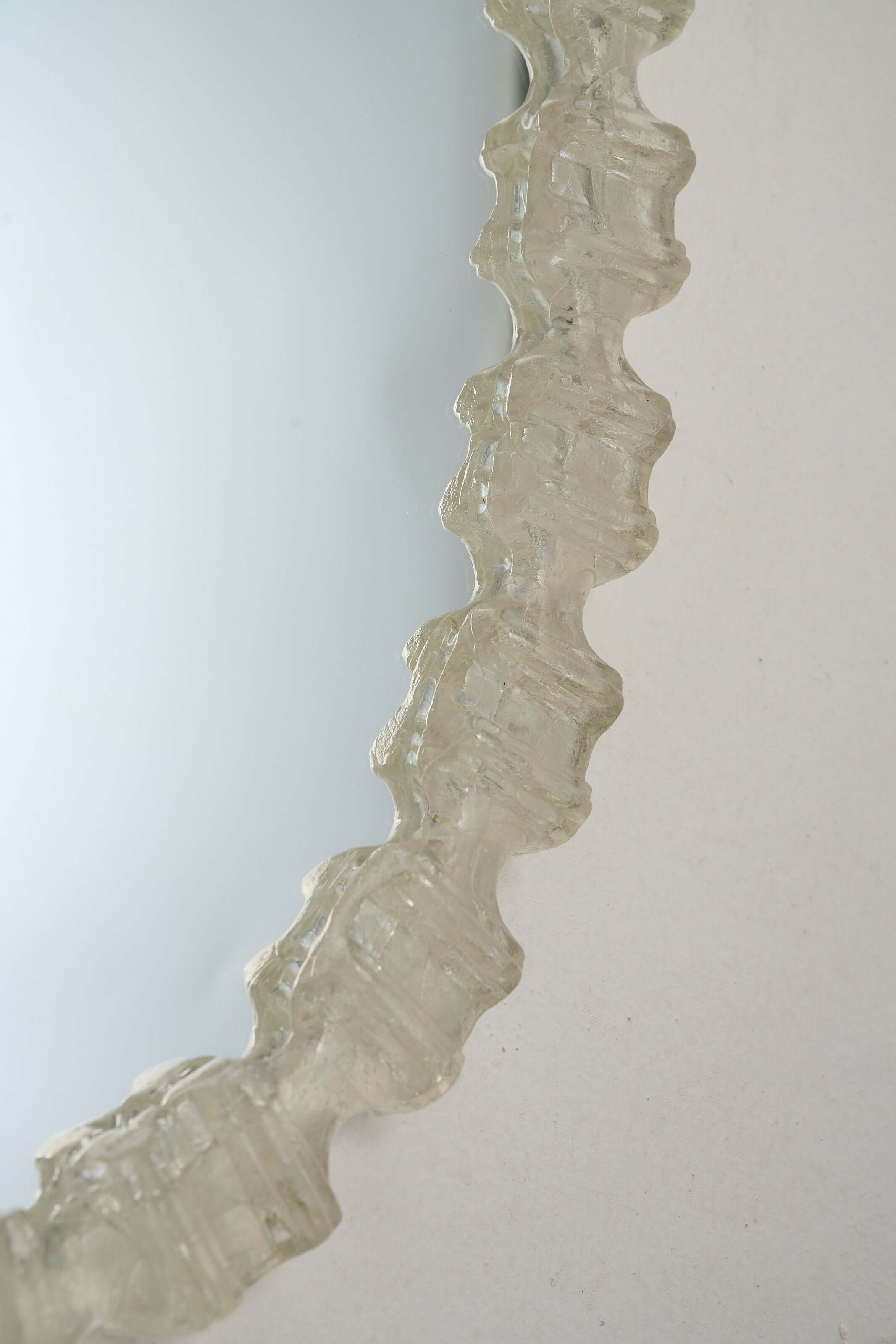 Close-up of the textured frame of an Oval Cast Plexiglass Mirror showcasing the unique geometric edge pattern.