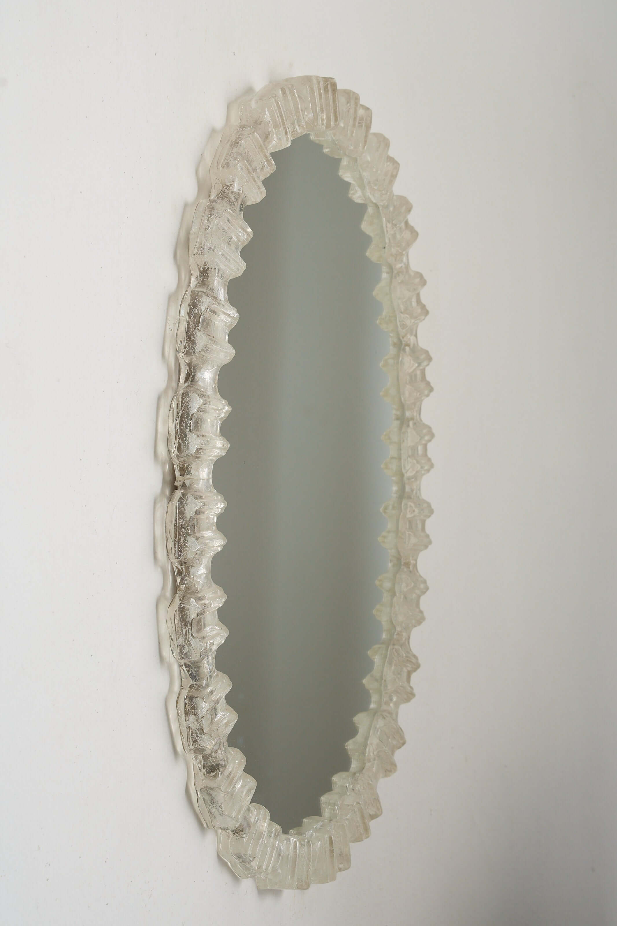 Oval Cast Plexiglass Mirror with a textured, block-like frame reflecting soft light on a white wall.