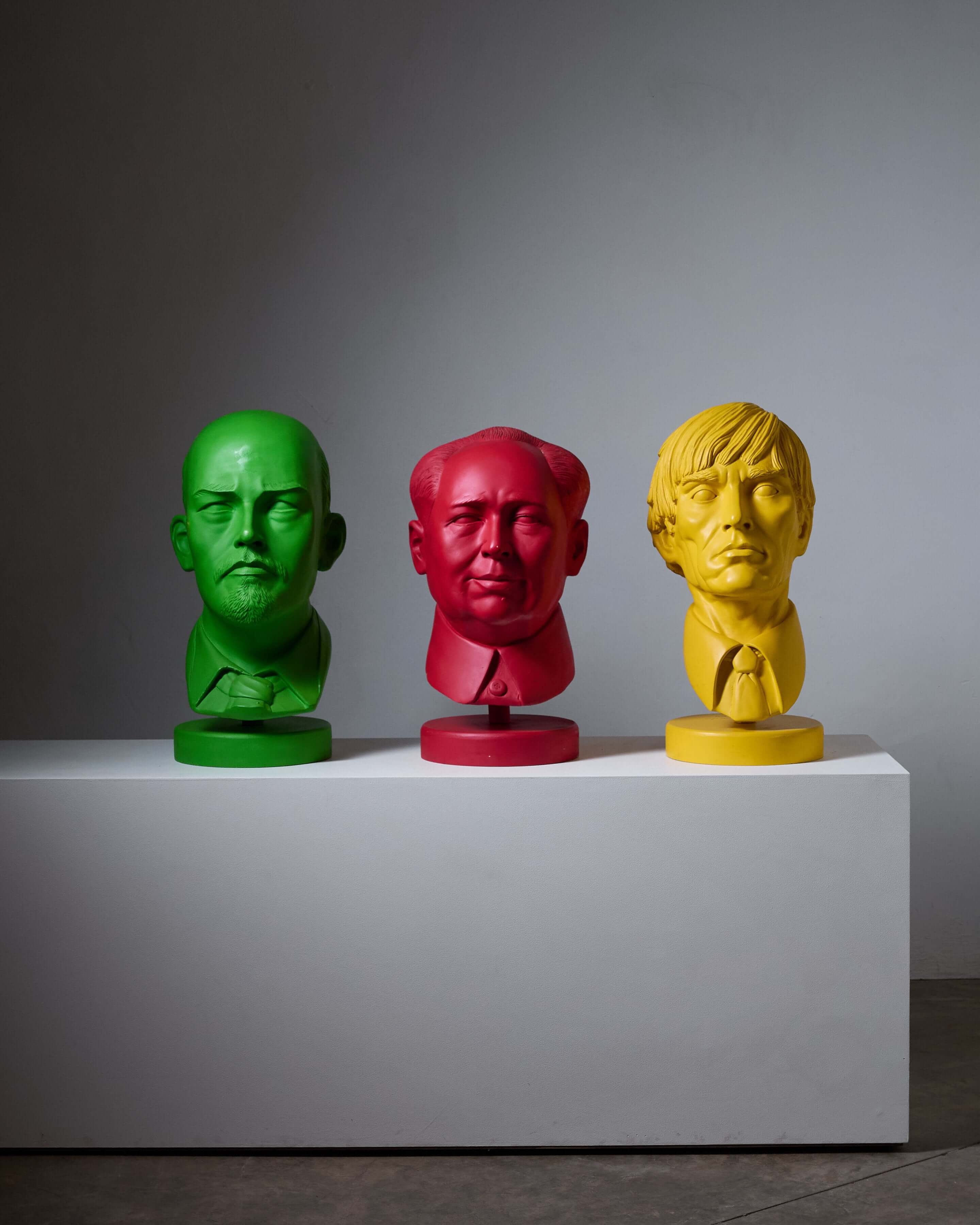 Three colorful bust sculptures in green, red, and yellow displayed on a white pedestal.