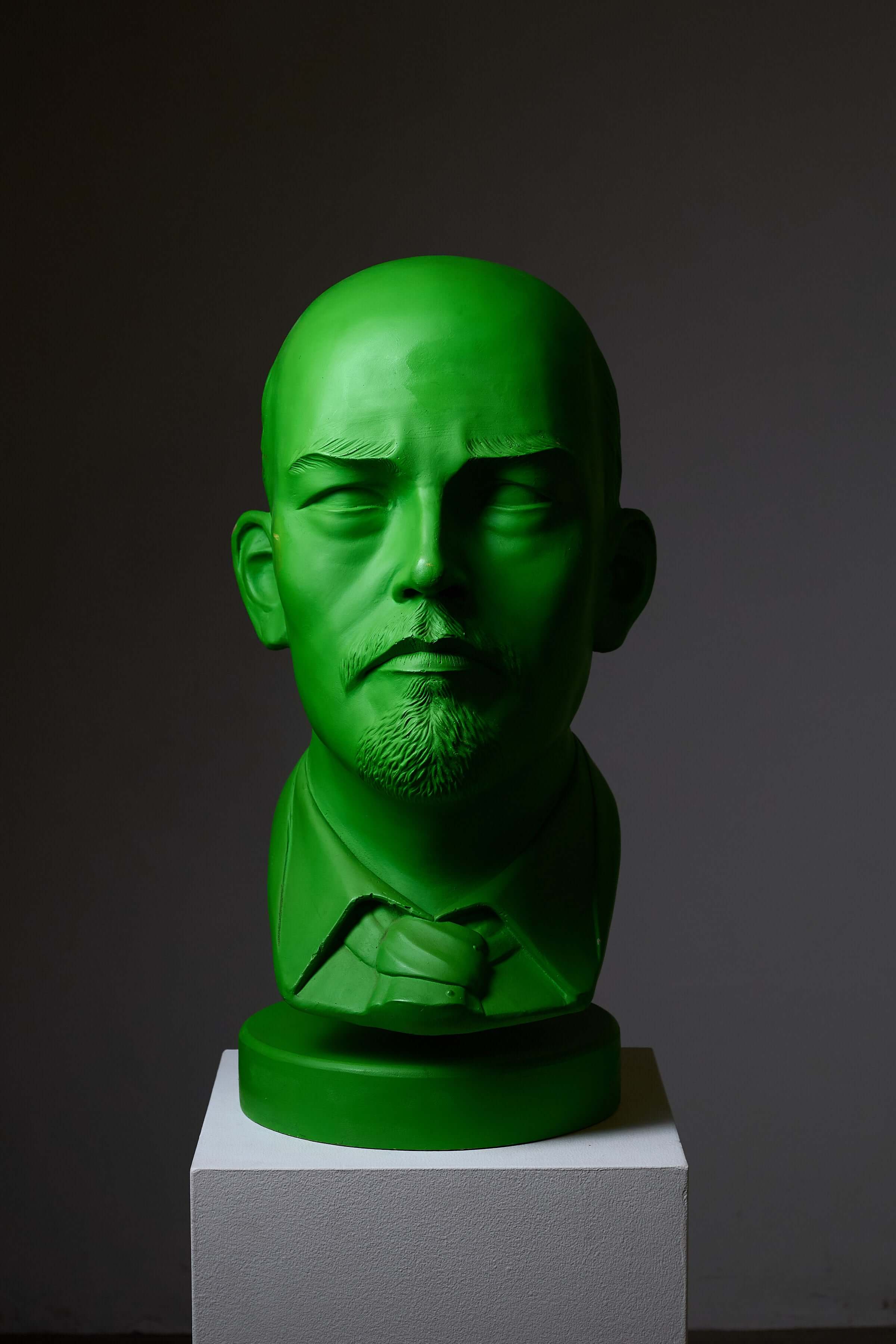 Vladimir Lenin Sculpture by Leonardo in vibrant green color displayed on a pedestal against a dark background.