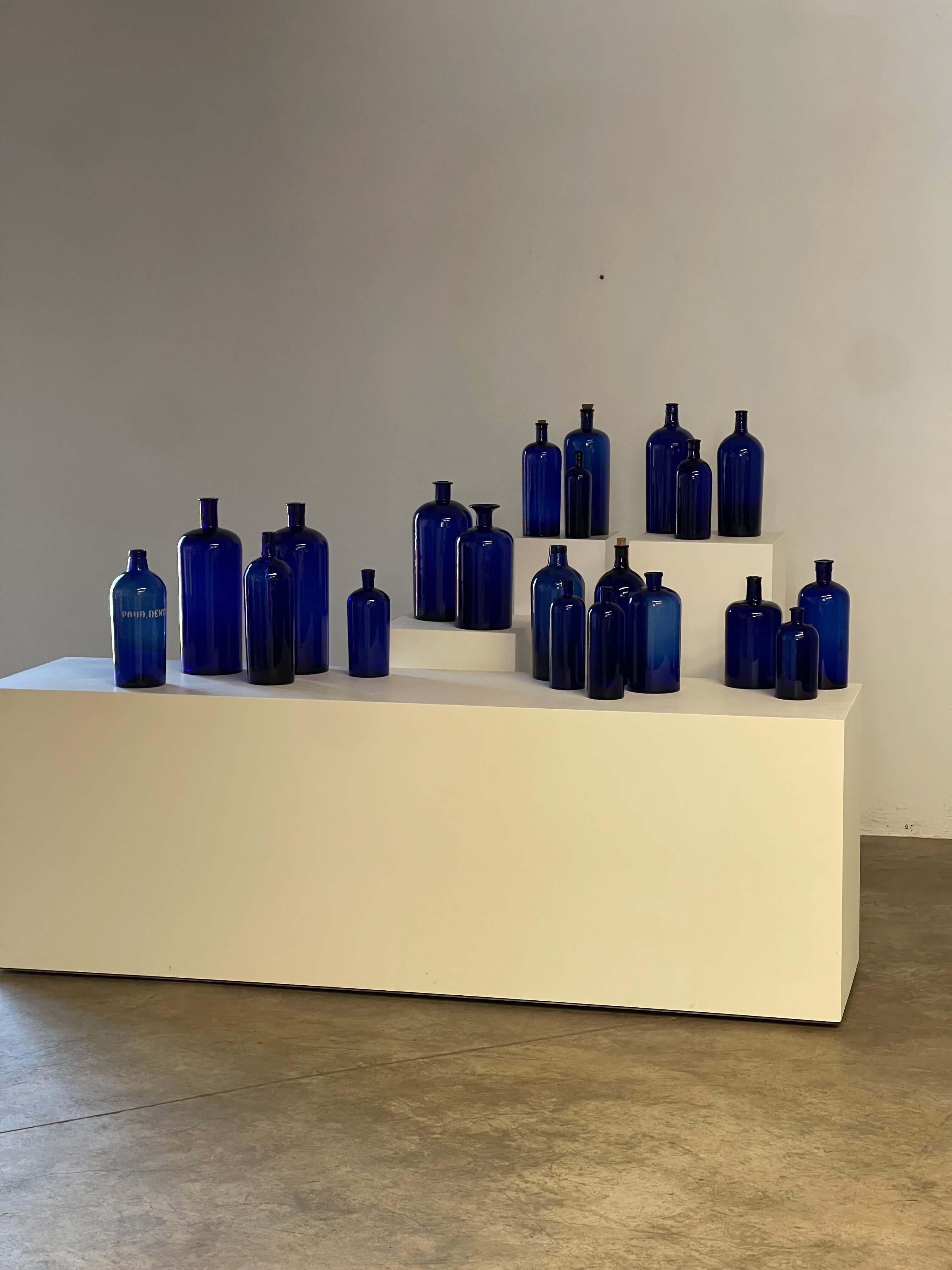 Collection of Antique Cobalt Blue Essence and Apothecary Bottles displayed on a white pedestal.
