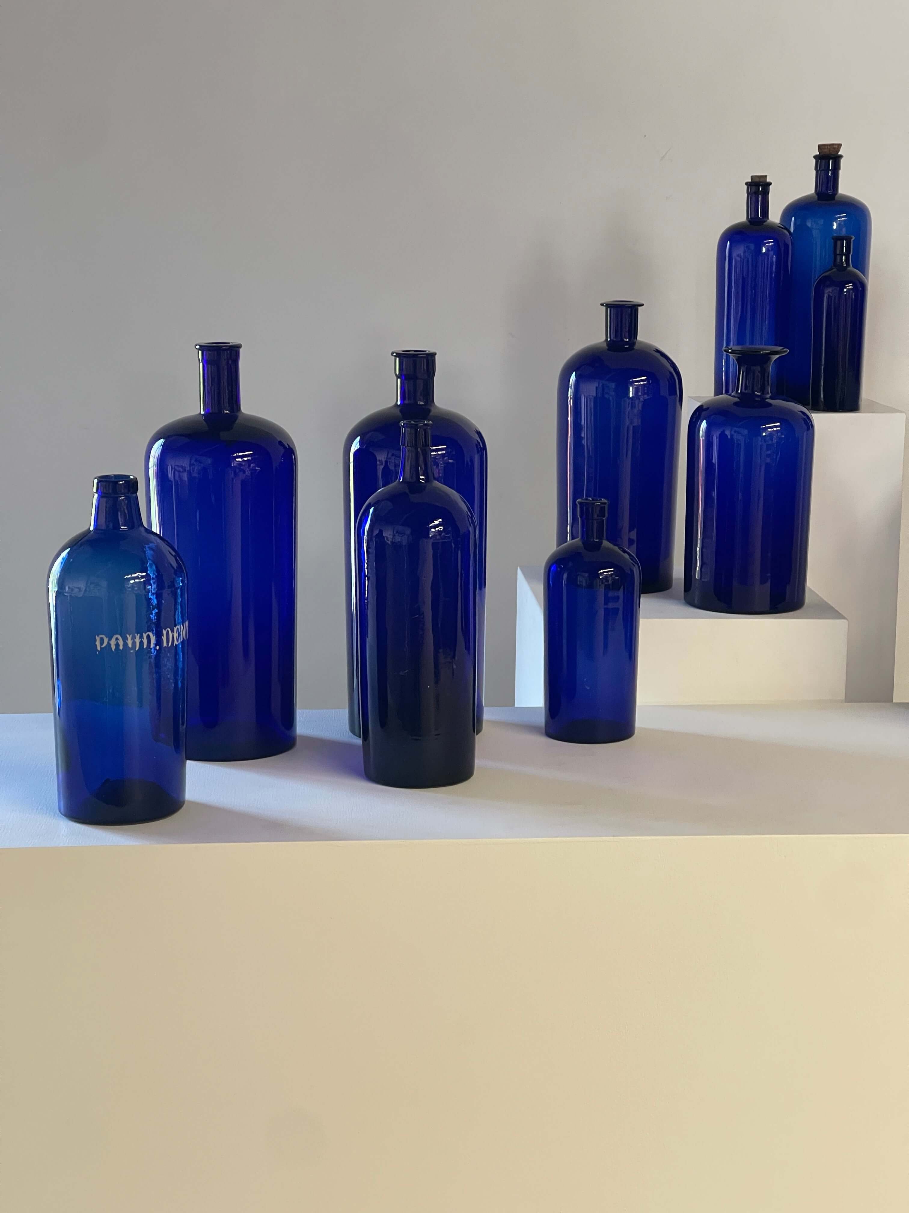 Collection of Antique Cobalt Blue Essence and Apothecary Bottles displayed on a white surface.