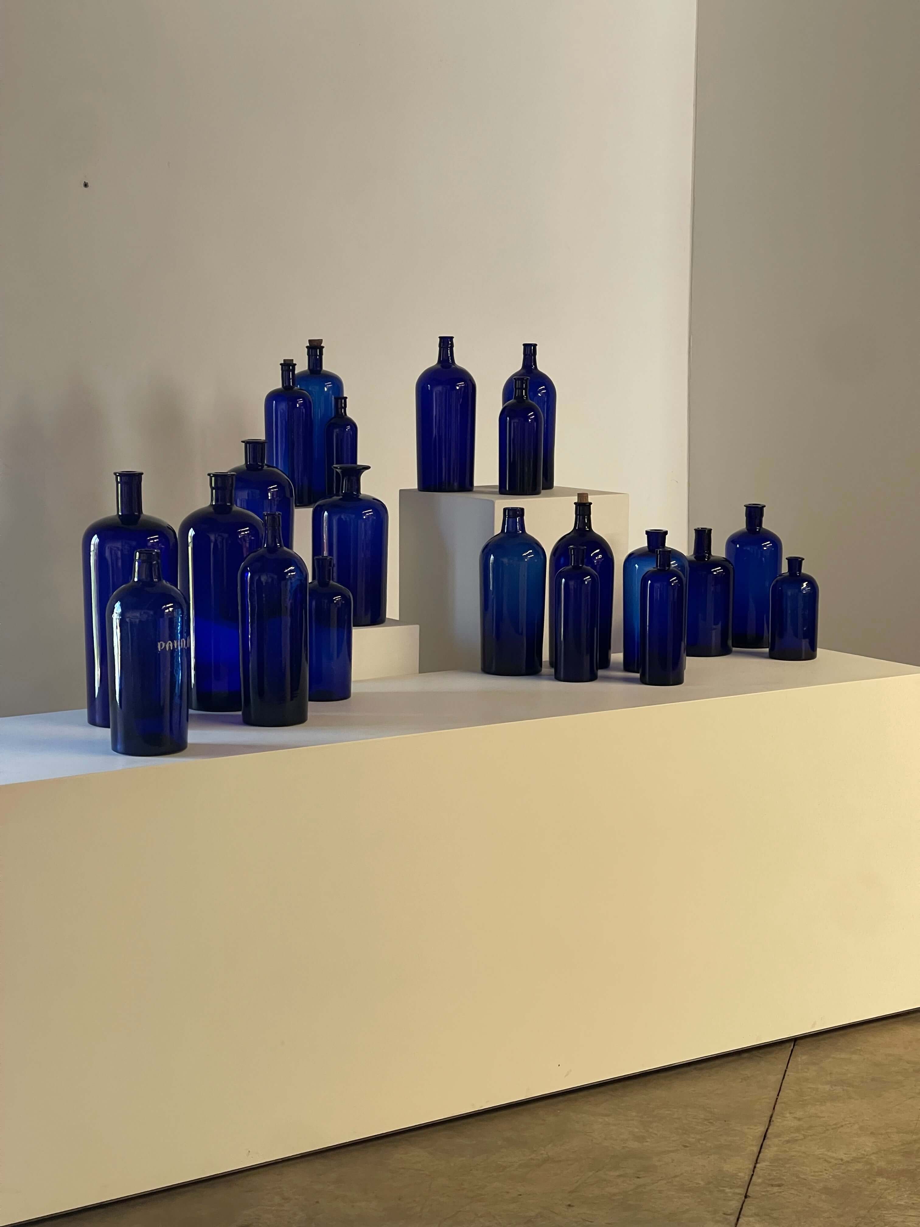 Collection of Antique Cobalt Blue Essence and Apothecary Bottles displayed on a white shelf, showcasing blue glass designs.