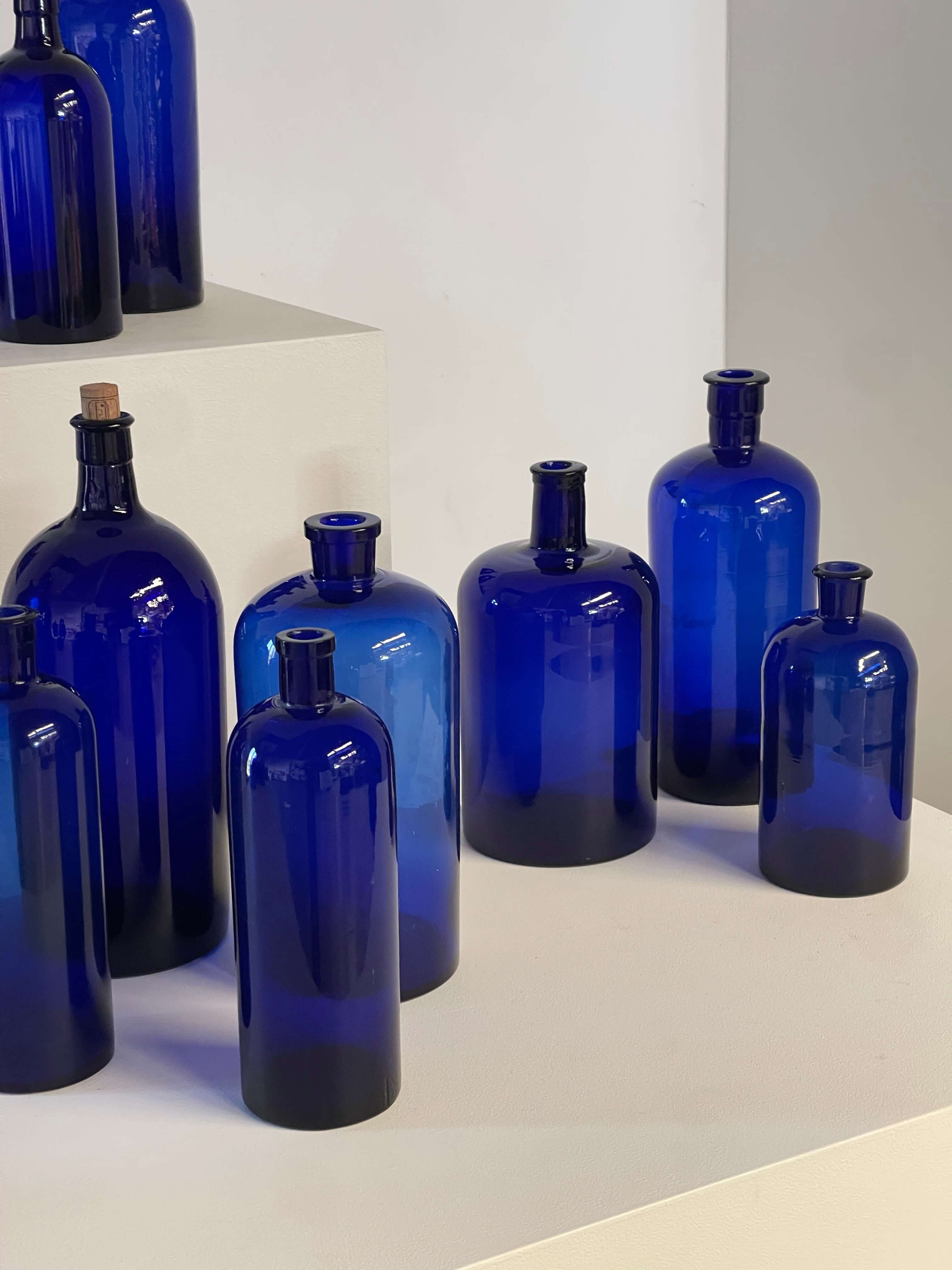 Collection of Antique Cobalt Blue Essence and Apothecary Bottles displayed on a white pedestal.