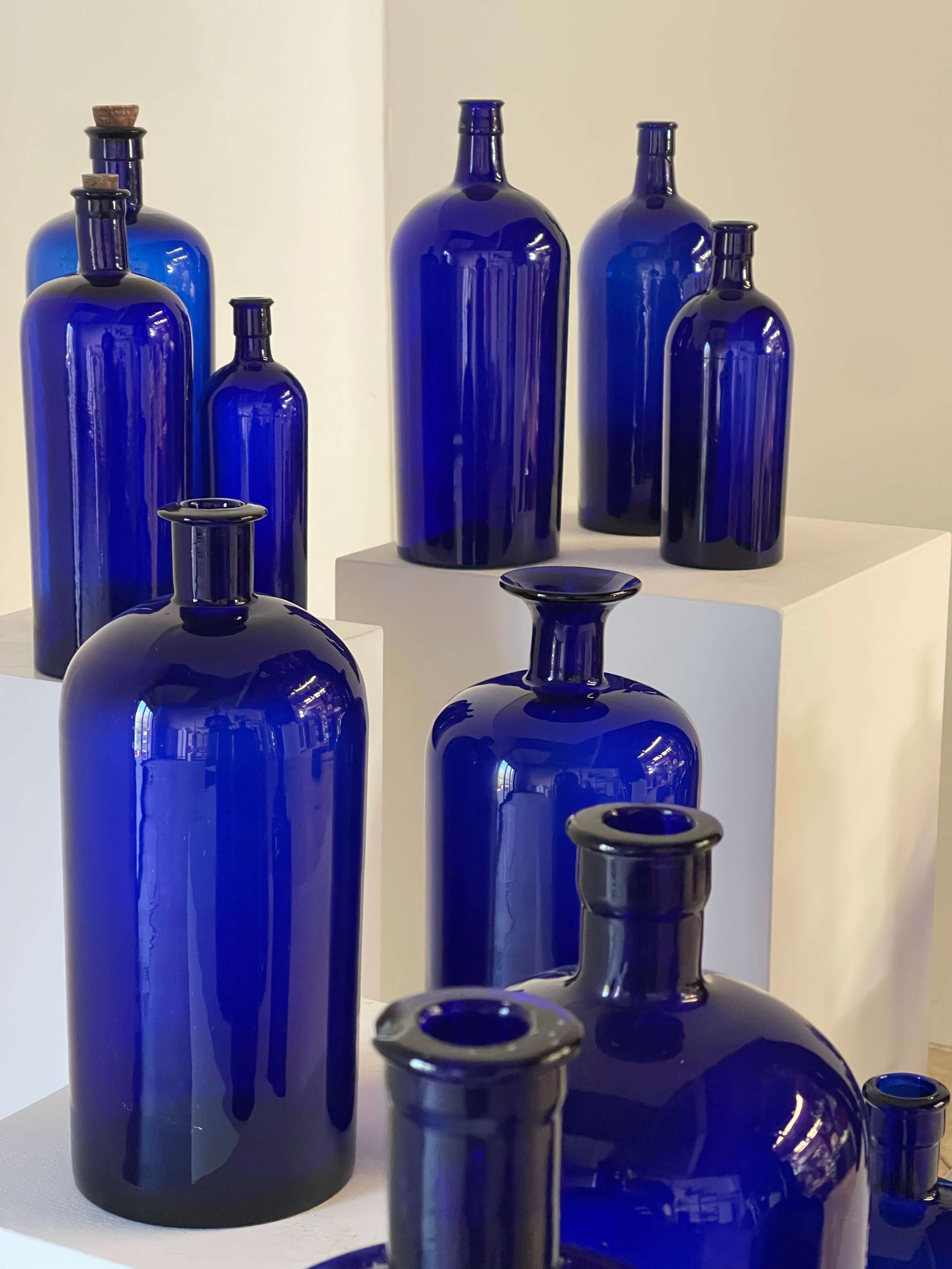 Collection of Antique Cobalt Blue Essence and Apothecary Bottles displayed on pedestals.